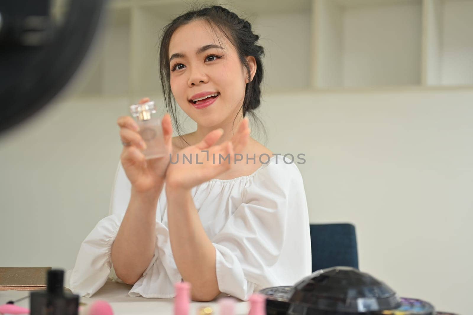 Pretty asian woman beauty blogger showing perfumes to camera while recording video and giving advices for her followers . by prathanchorruangsak
