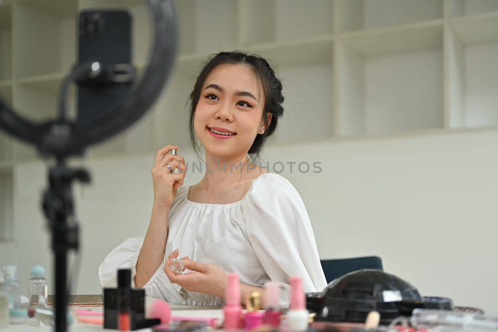 Charming female beauty blogger spraying perfume on her neck while recording video in dressing room. by prathanchorruangsak