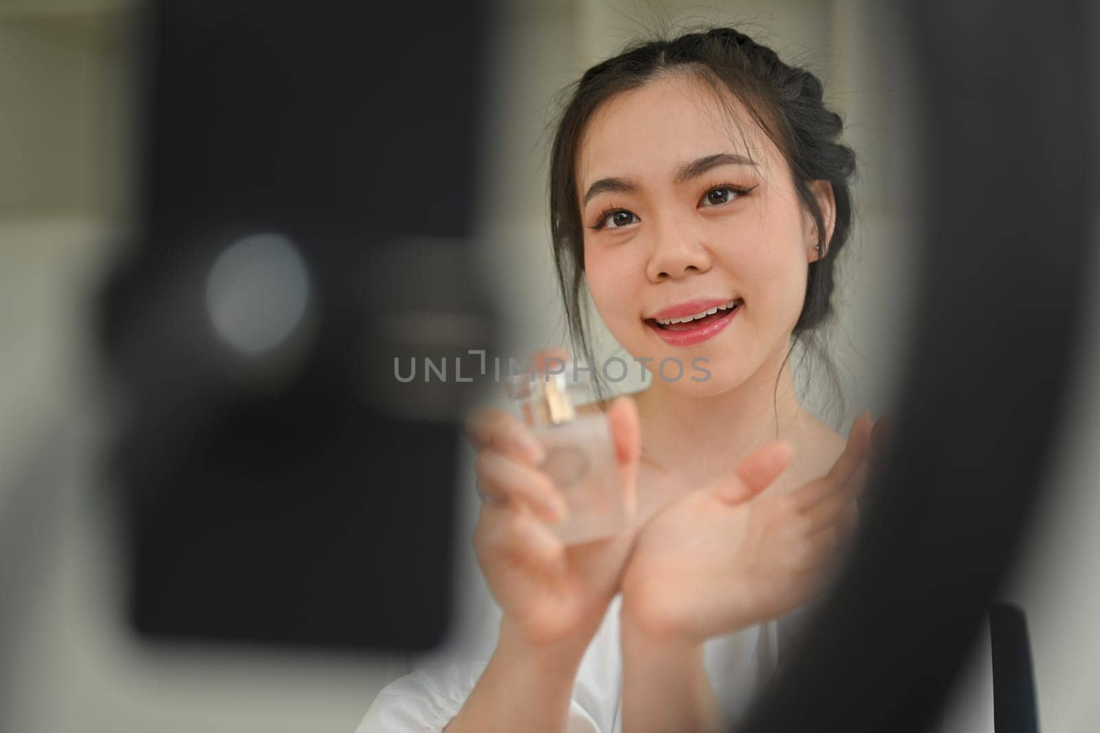 Asian woman beauty blogger showing perfumes to camera while making new video for her beauty channel. by prathanchorruangsak