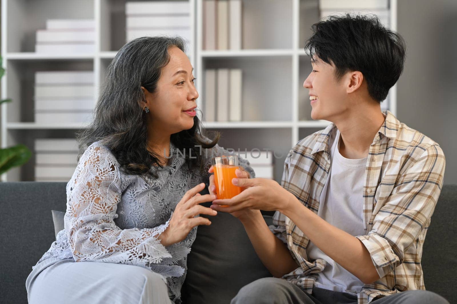 Young adult asian man giving glass of orange juice to grandmother. Family, happiness, generation and domestic life by prathanchorruangsak