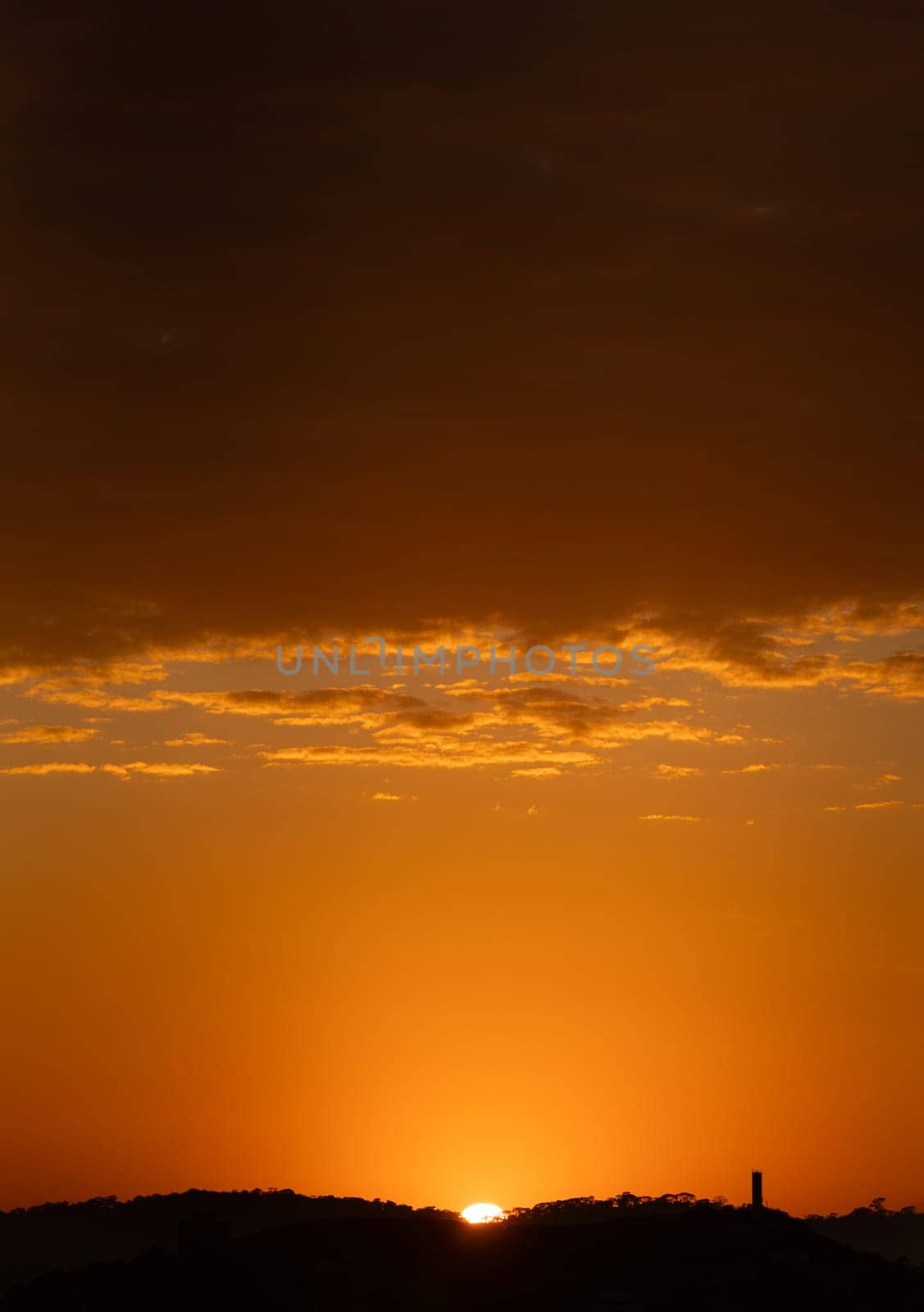 Stunning sunrise behind mountains with a tower silhouette under a cloudy orange sky, providing an ideal background with text space.