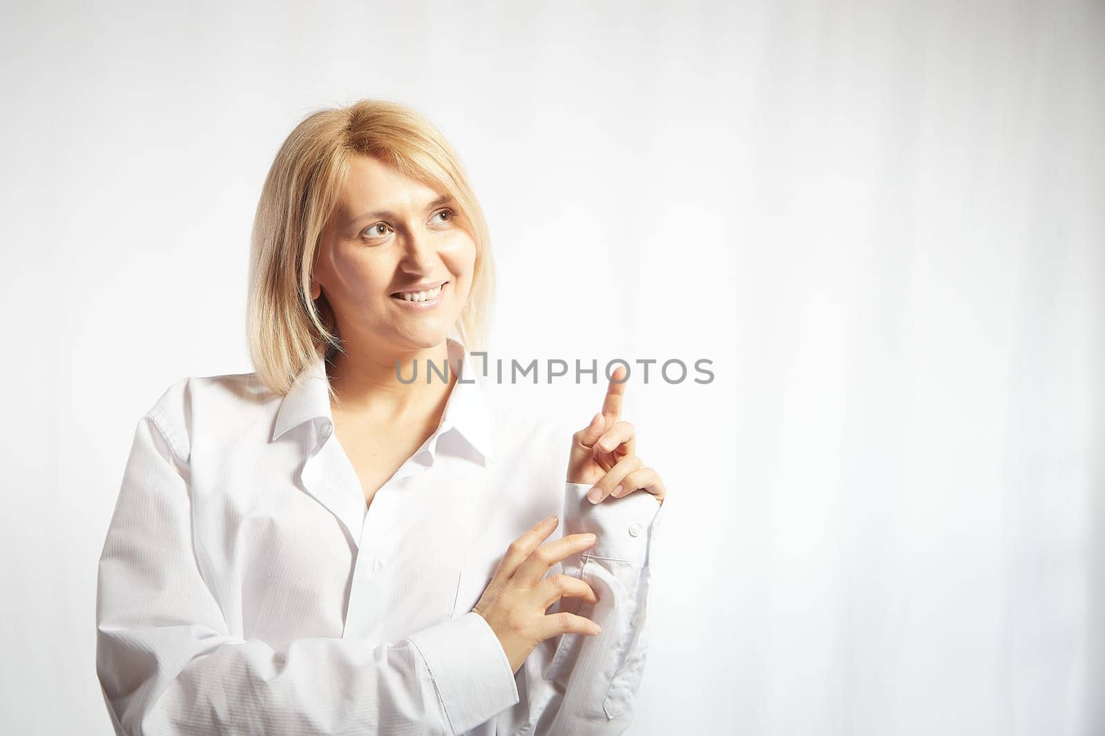 Portrait of a pretty blonde smiling woman posing on white background and pointing somewhere. Happy girl model in white shirt posing in studio. Copy space