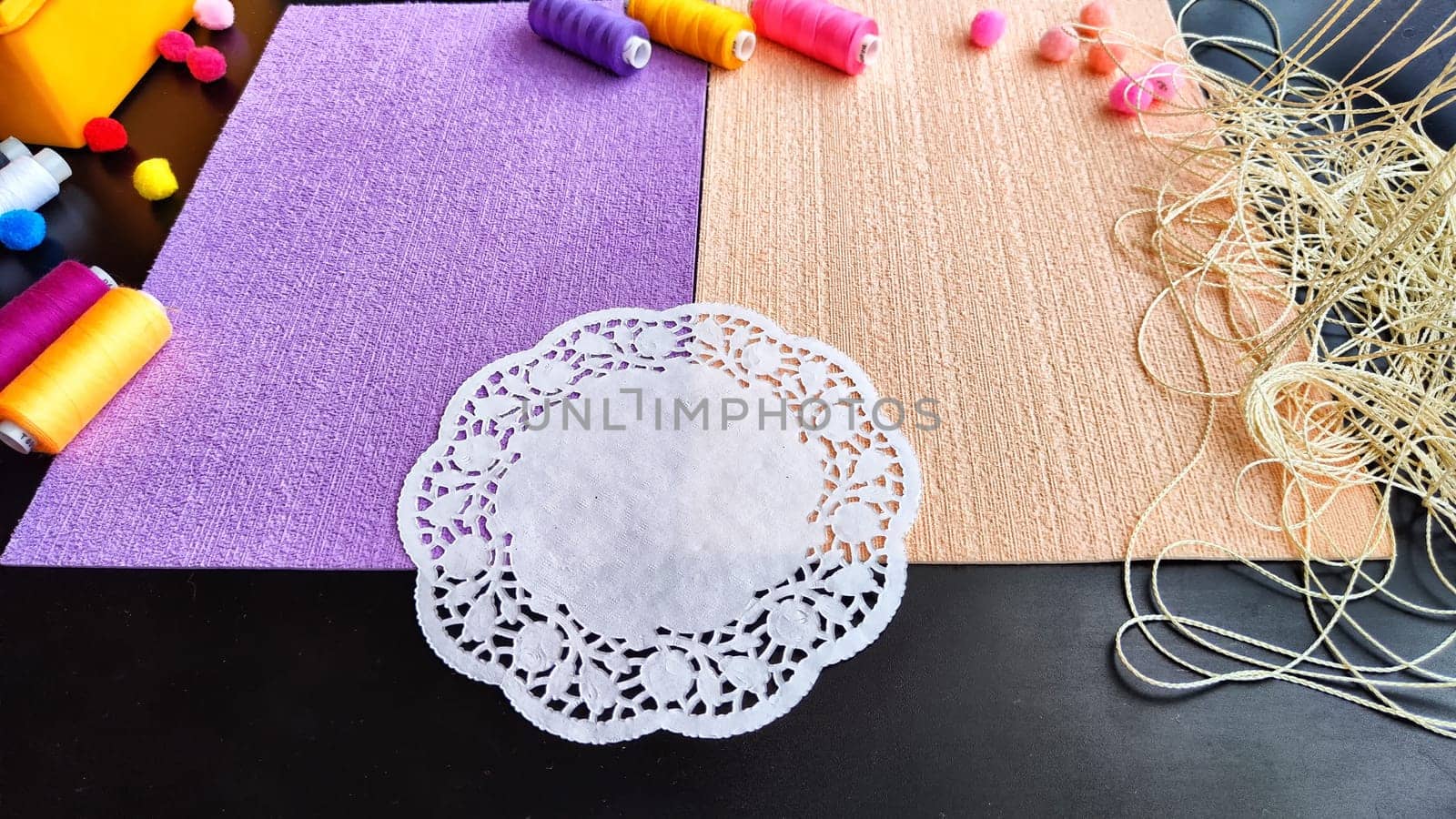 Abstract background with texture and frame with beige and lilac or purple velvet paper, a white napkin, colored spools of treateds and copy space. Top view. Hand made and sewing