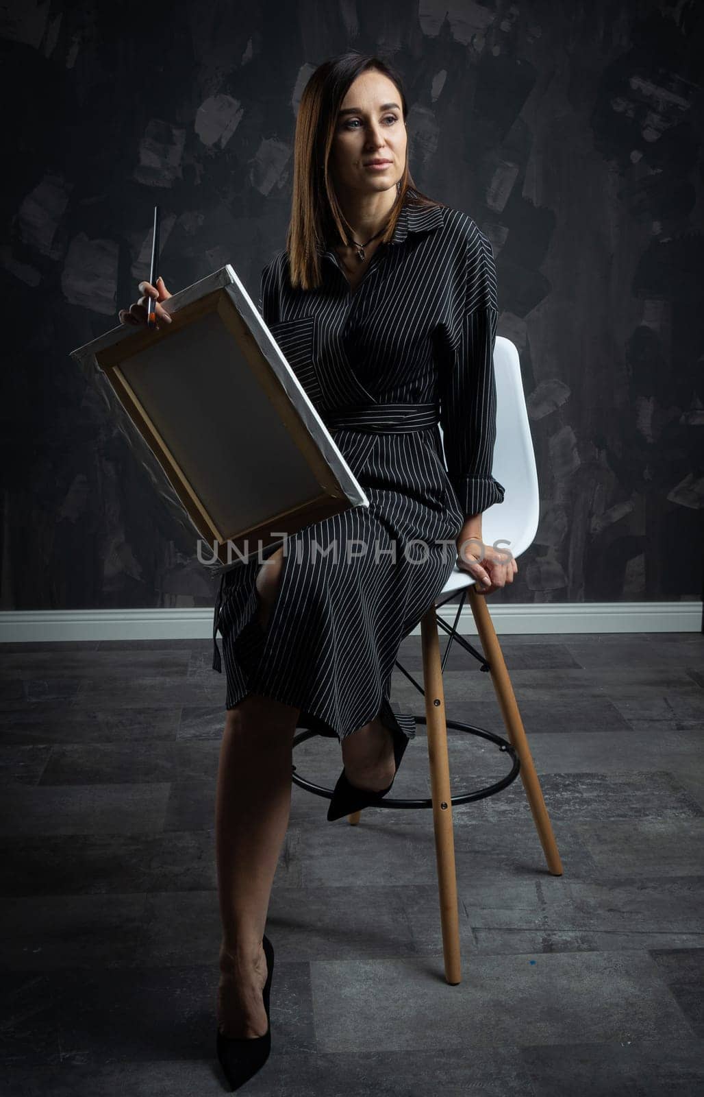 a young brunette female artist stands behind an easel. photo shoot on a black background in the studio