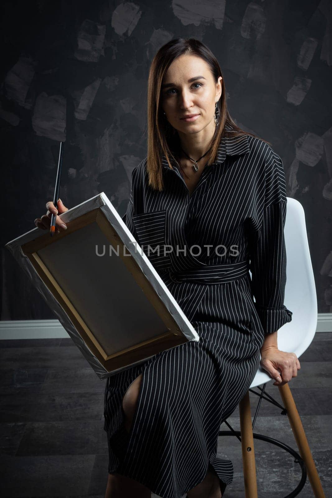 a young brunette female artist stands behind an easel. photo shoot on a black background in the studio