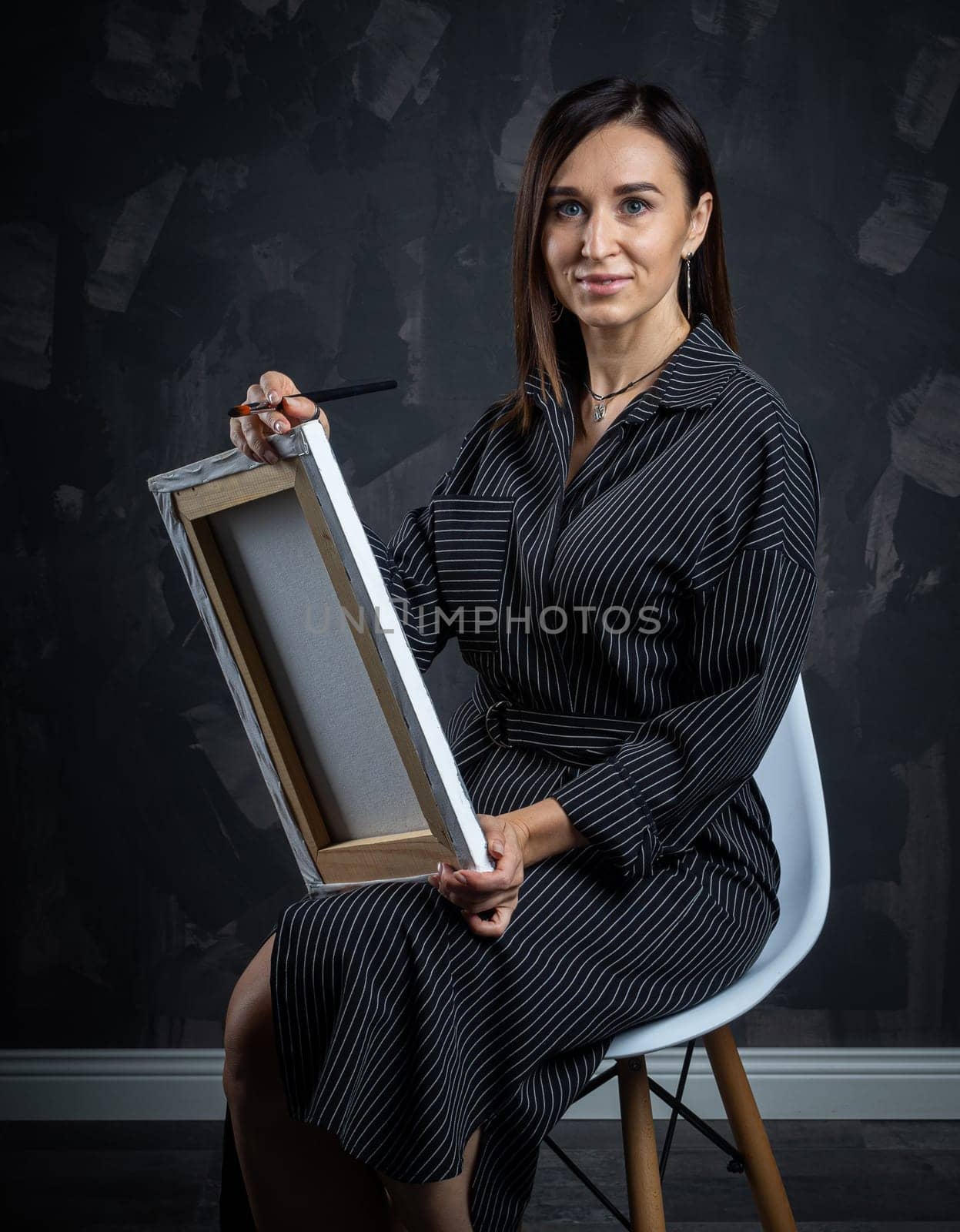 a young brunette female artist stands behind an easel. photo shoot on a black background in the studio