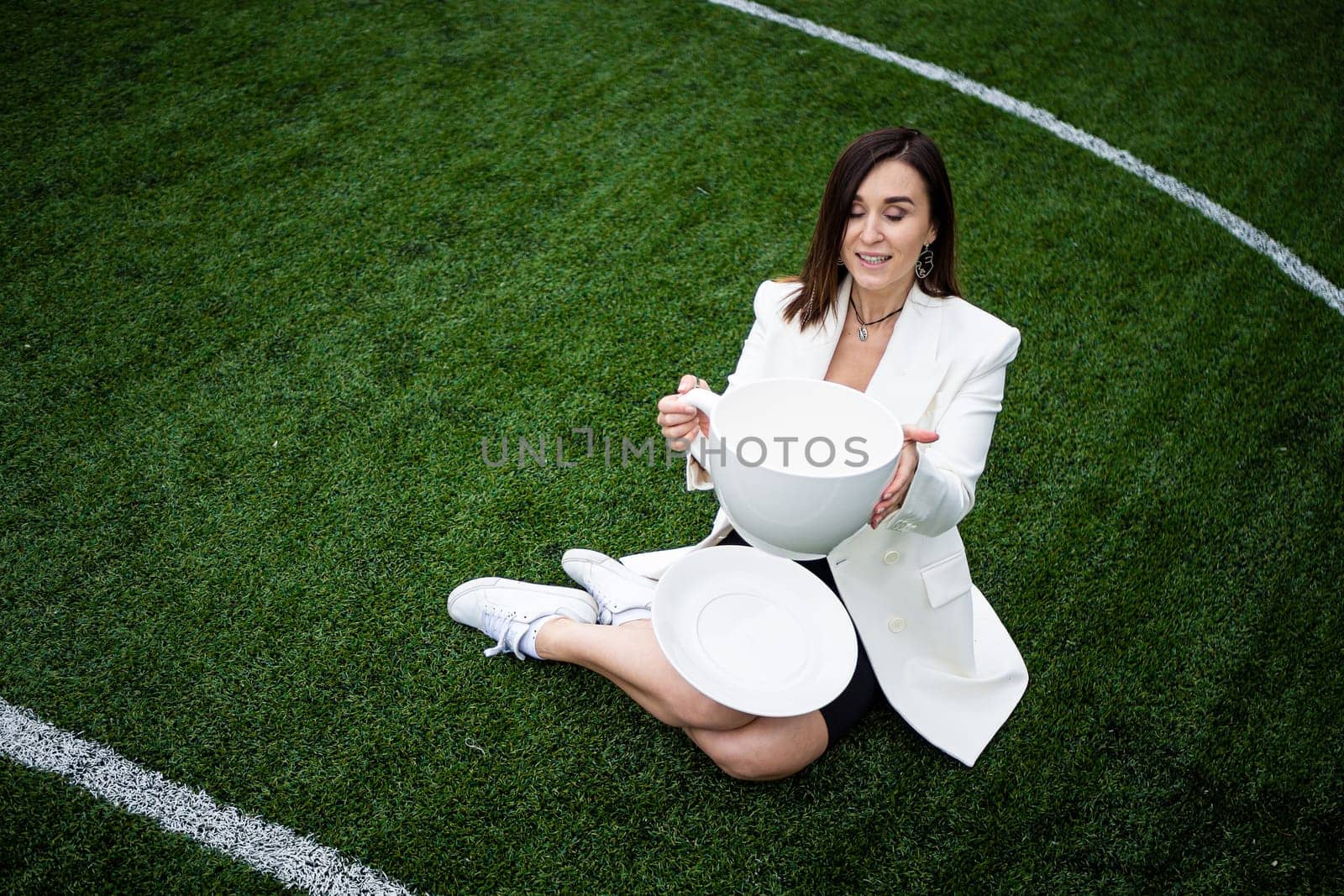 A business woman with a large cup, sitting on a green lawn in the park. The concept of an office worker on a picnic.
