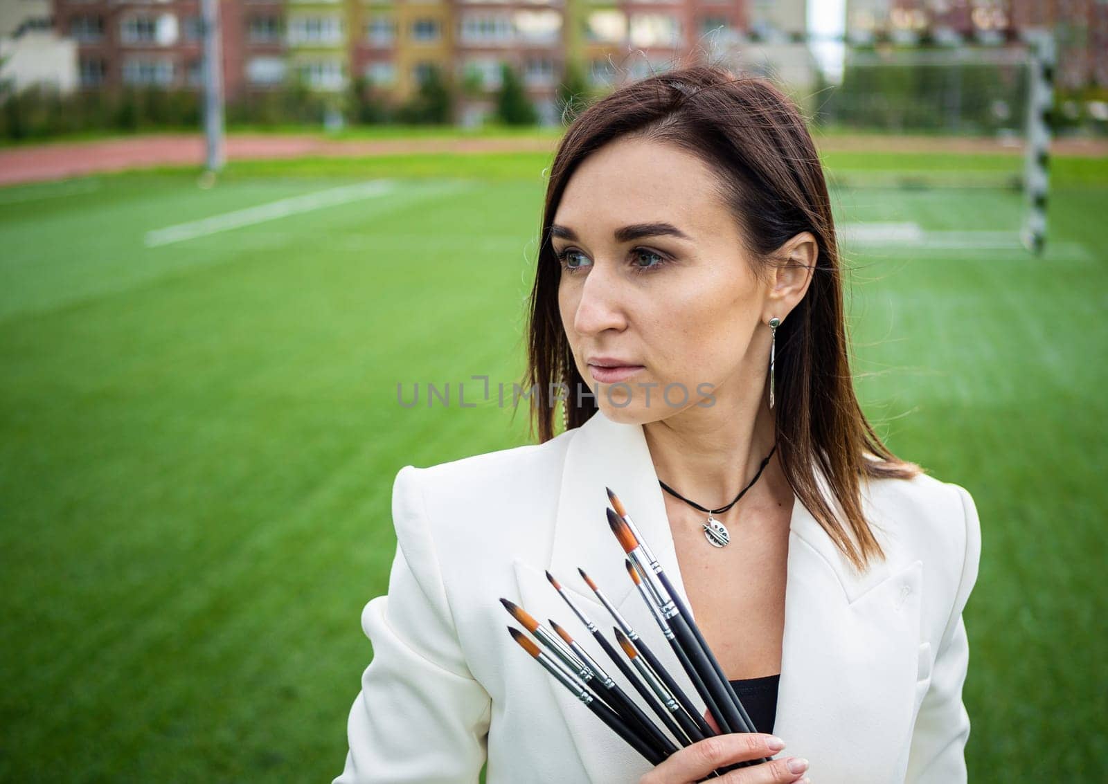 Brunette, female artist paints in nature. She has paint brushes in her hands.