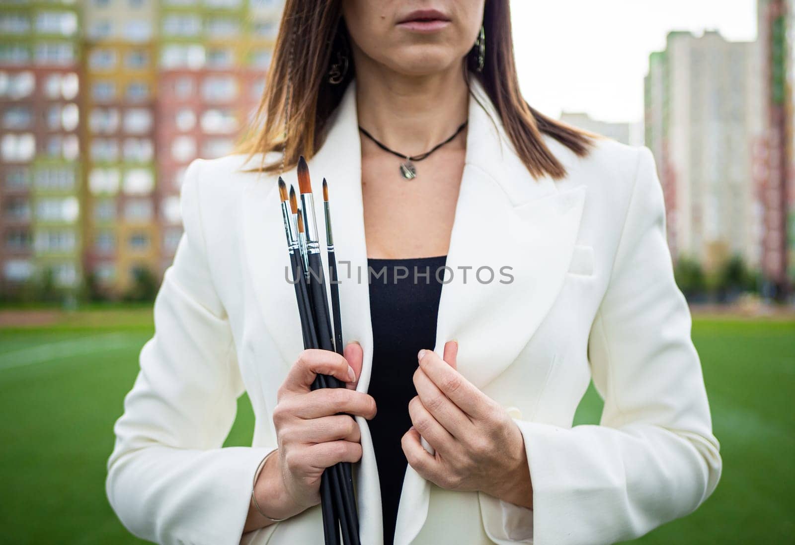 Brunette, female artist paints in nature. She has paint brushes in her hands.