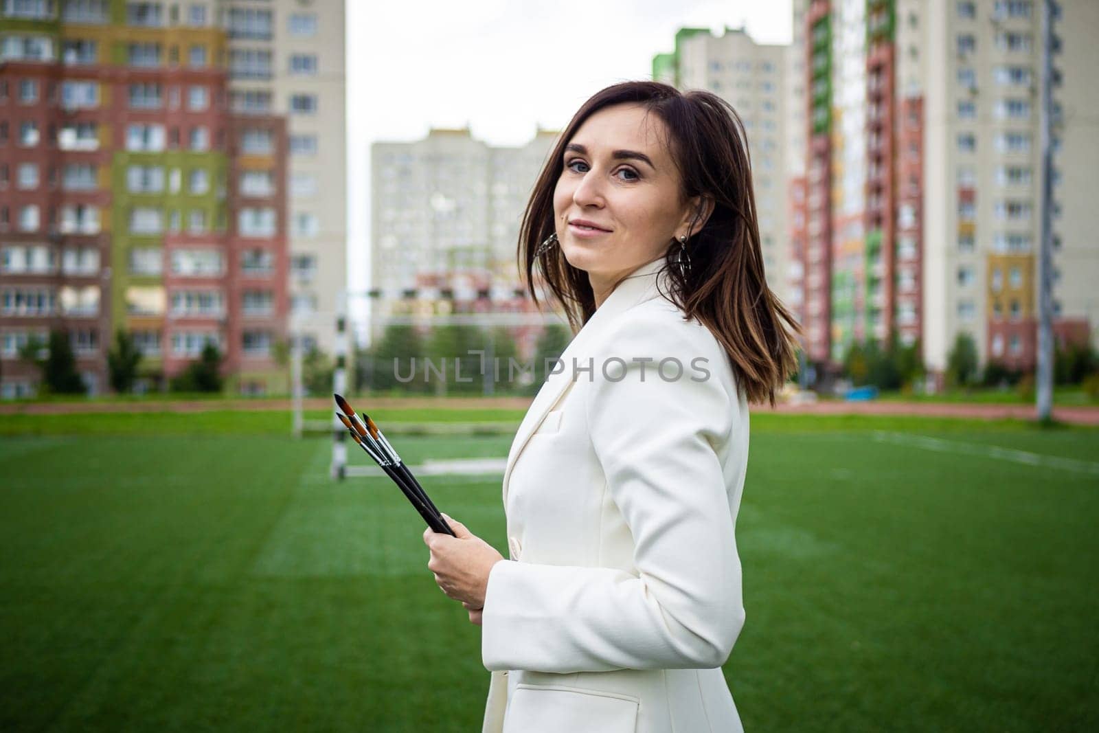 Brunette, female artist paints in nature. She has paint brushes in her hands.