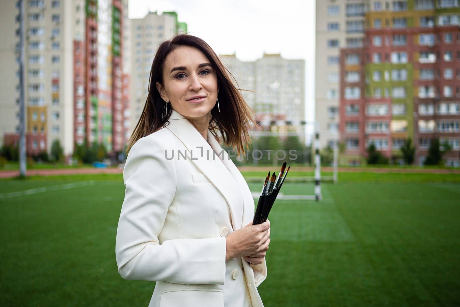 Brunette, female artist paints in nature. She has paint brushes in her hands.