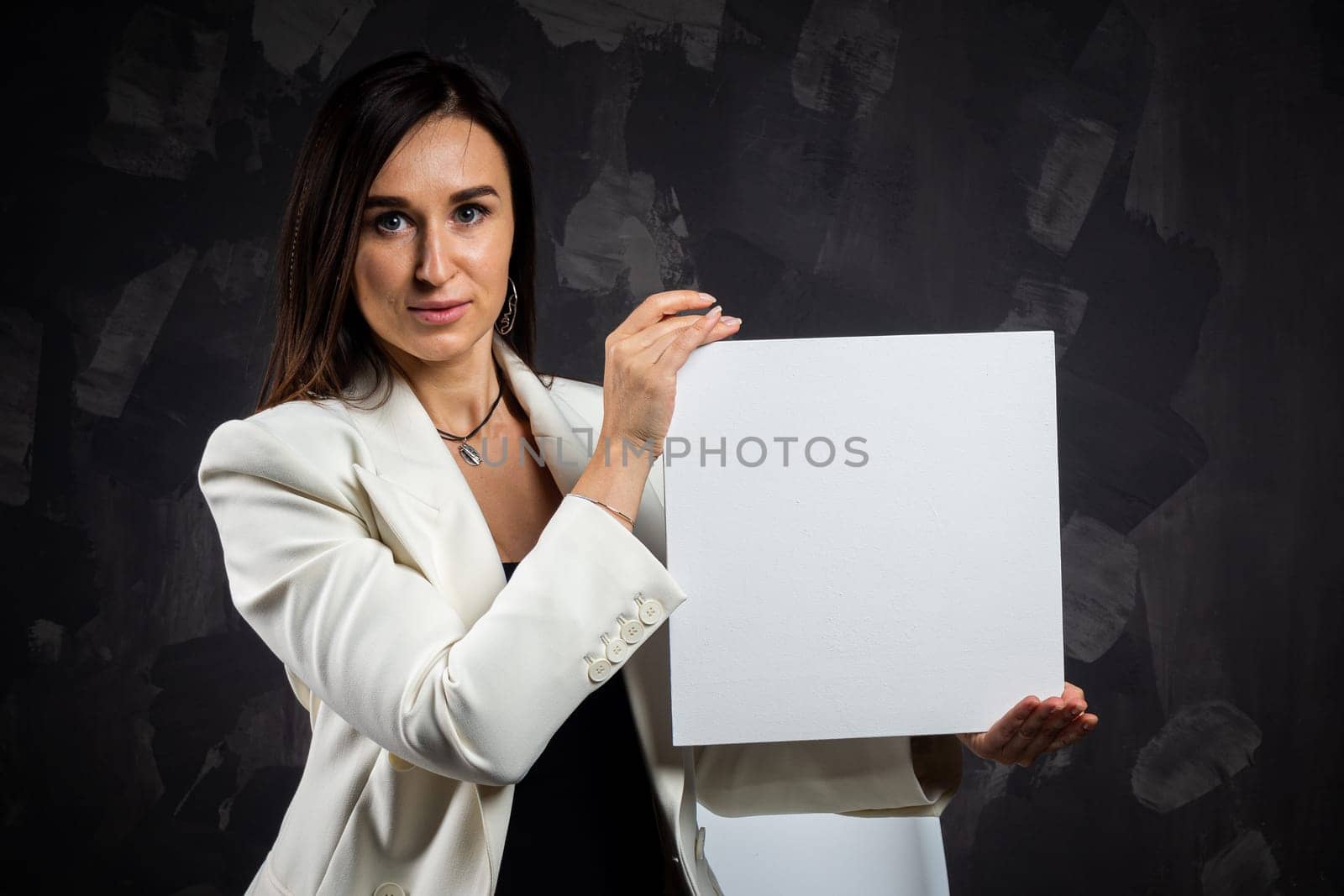 A business woman holds an empty sign in front of the camera. Shot in the studio on a dark background.