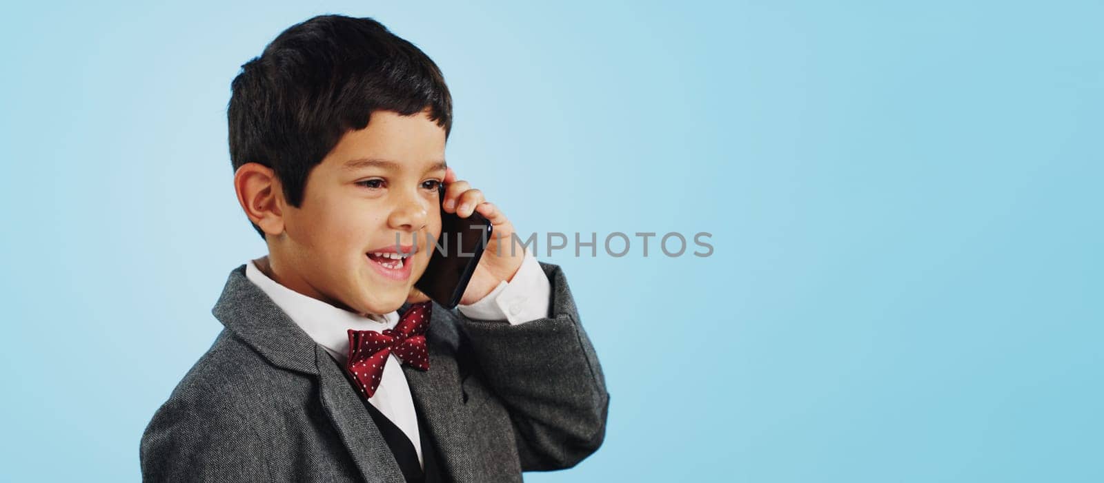 Child, talking and boy with phone call in studio, blue background and mockup with telephone chat or conversation. Calling, kid and speaking with cellphone communication or discussion with mobile.