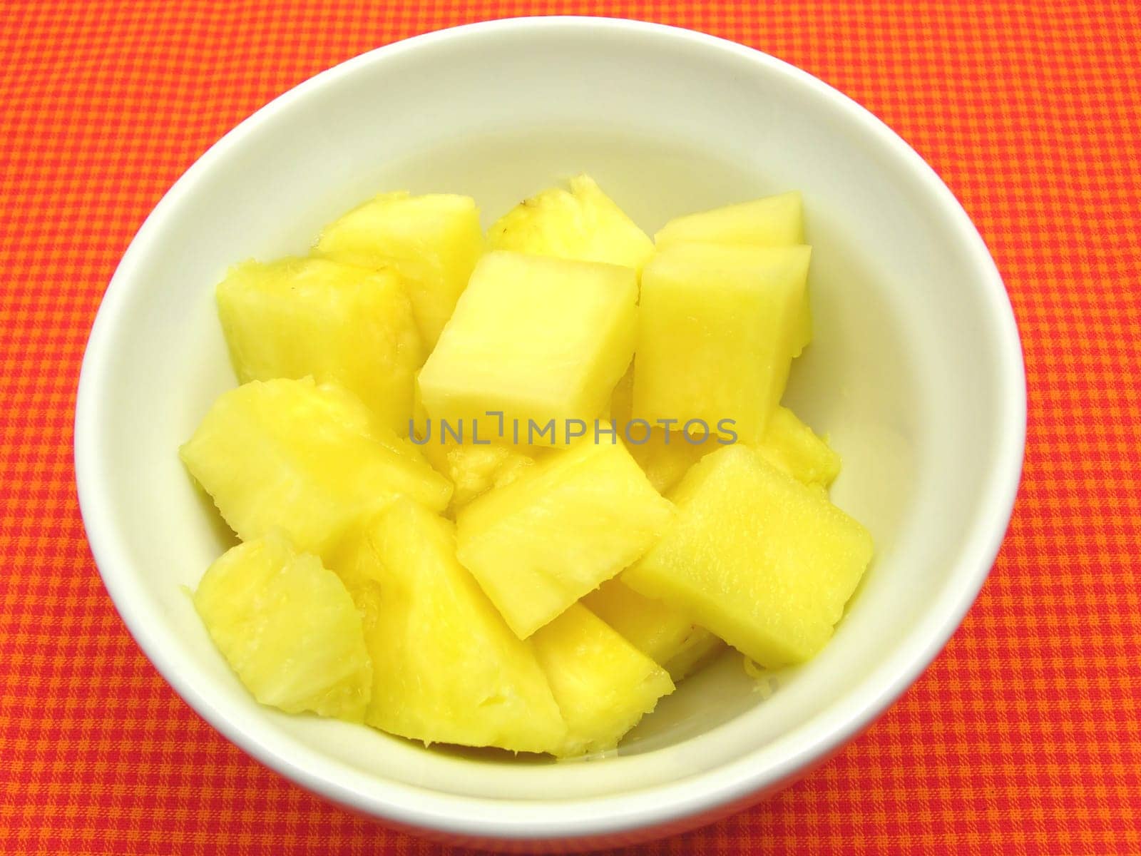 Pineapple pieces in a white porcelain bowl on a red-checkered base