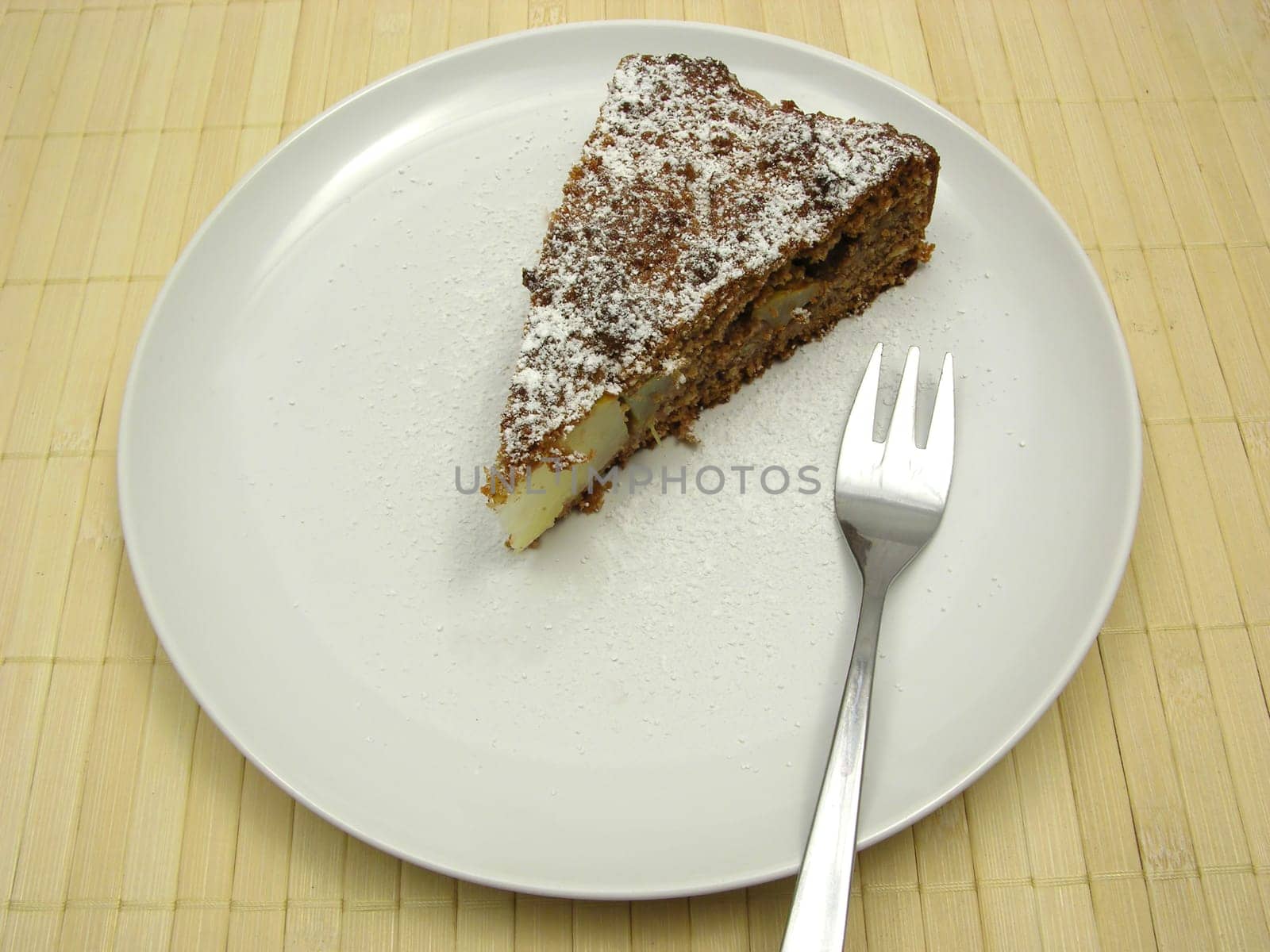 A piece of pear cake on a white plate dusted with powdered sugar