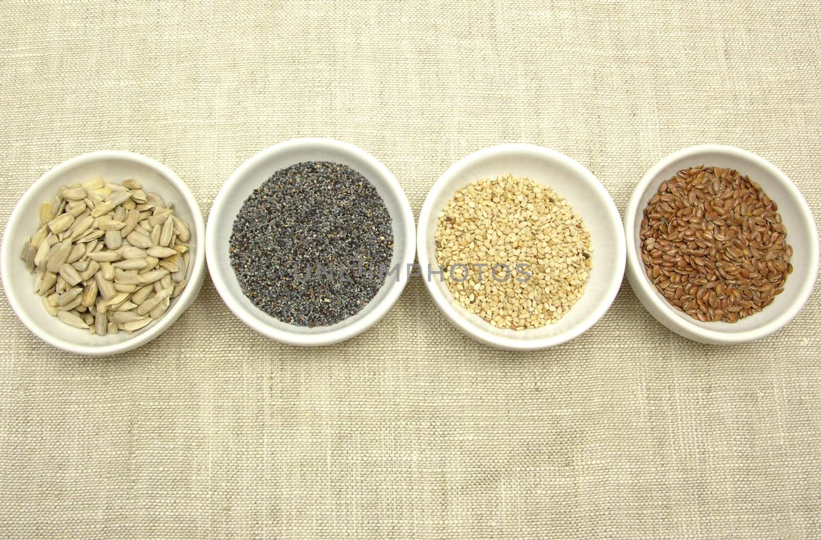 Four bowls with different seeds on a beige background