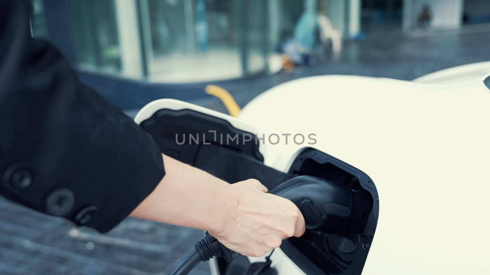 Progressive businesswoman install charger plug from charging station to his electric car before driving around city center. Eco friendly rechargeable car powered by sustainable and clean energy.