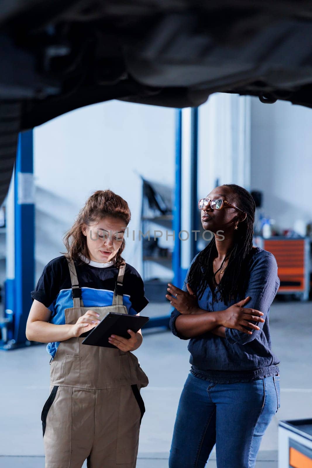 Repairman in car service orders new tires for damaged vehicle using tablet. Engineer next to client looking online for components to replace old ones in malfunctioning suspended automobile