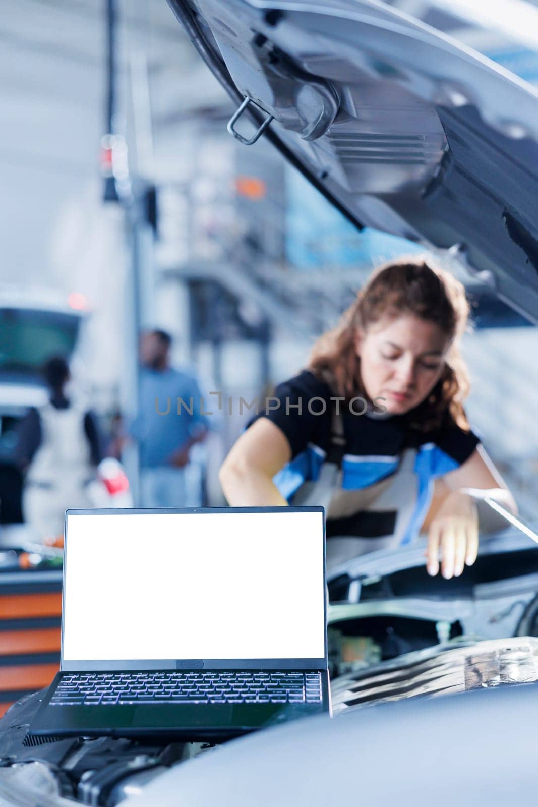 Mockup laptop with blurry background of serviceman changing old car gear oil with new one in repair shop. Isolated screen device and hardworking woman in garage using equipment to do vehicle checkup