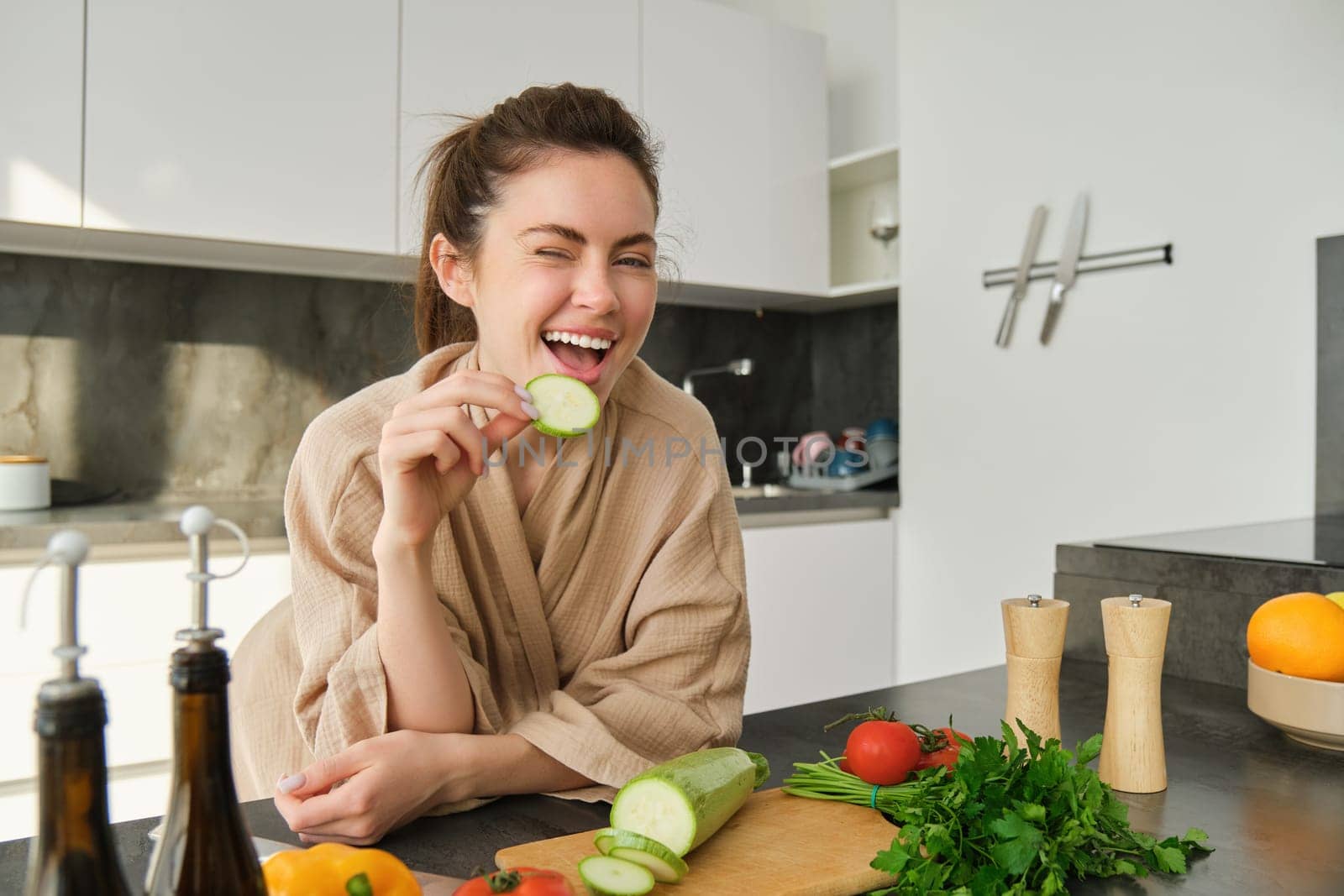 Portrait of brunette woman, wife cooking at home, making dinner, posing near chopping board in kitchen with vegetables, holding zucchini.