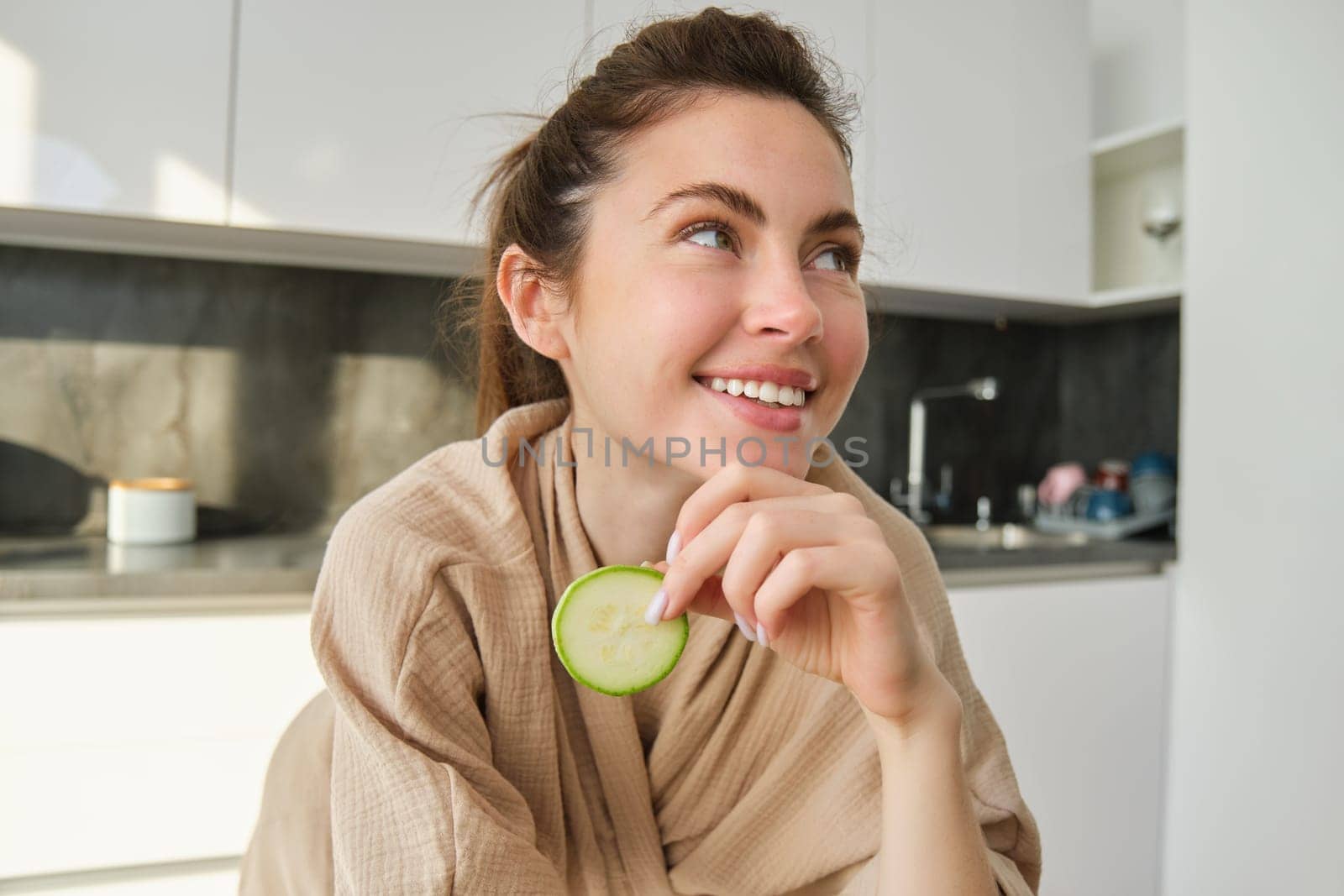 Portrait of happy, smiling young woman in the kitchen, cooking, chopping zucchini, holding vegetables and looking happy, preparing vegan food meal at home.