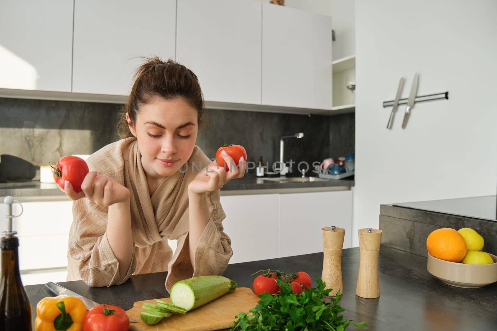 Portrait of woman cooking at home in the kitchen, holding tomatoes, preparing delicious fresh meal with vegetables, standing near chopping board by Benzoix