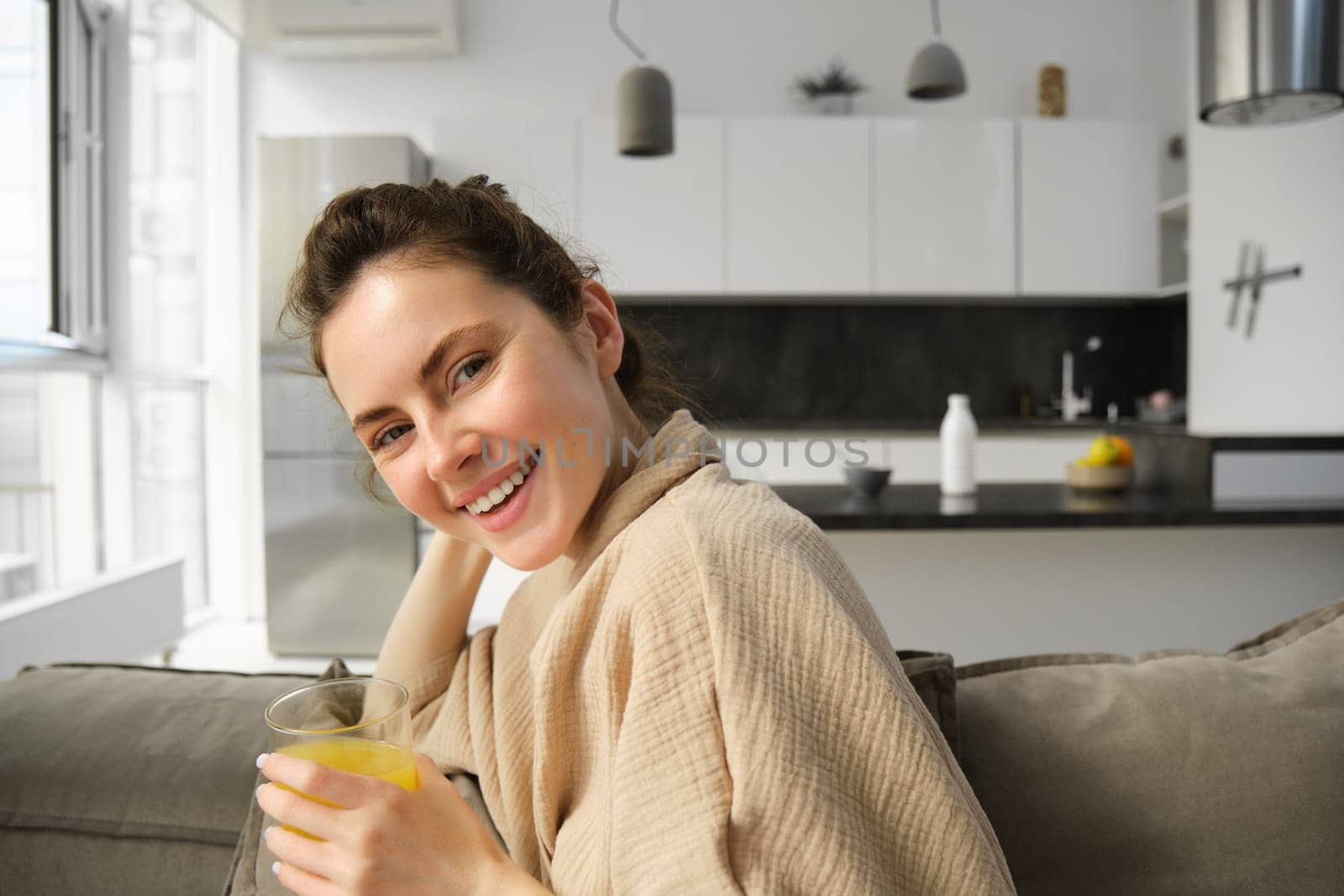 Women wellbeing and lifestyle. Beautiful young woman on sofa, drinking orange juice, relaxing at home on sofa, resting in the morning in living room.