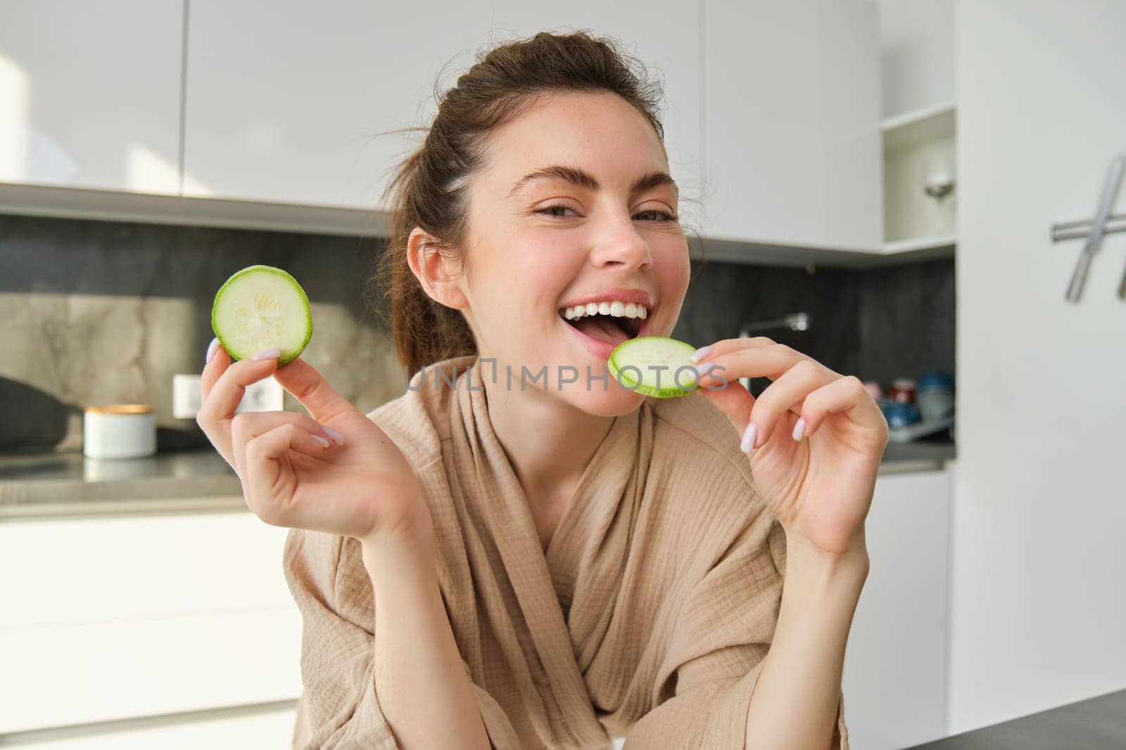 Portrait of happy, smiling young woman in the kitchen, cooking, chopping zucchini, holding vegetables and looking happy, preparing vegan food meal at home.