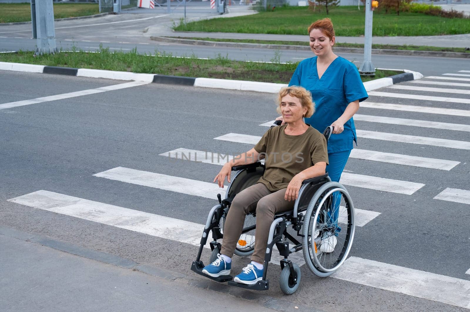 Red-haired nurse pushing an elderly woman in a wheelchair across the road