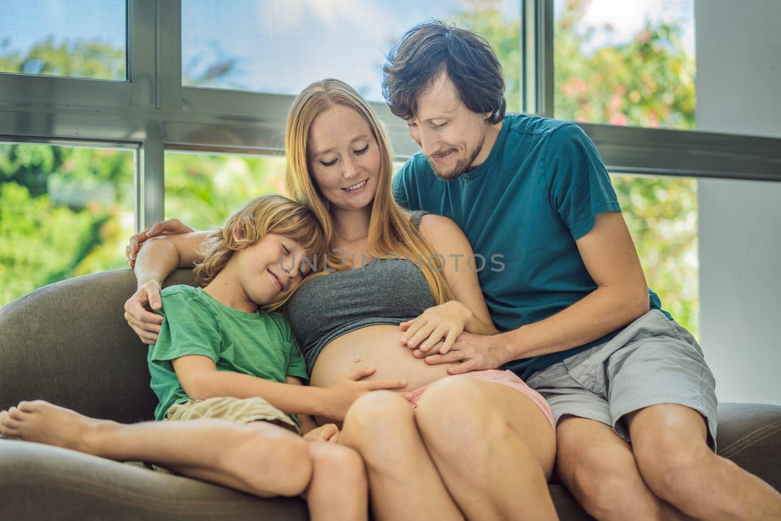 Expectant parents, mom, dad, and their eldest son share a heartwarming moment on the sofa, discussing the exciting journey of pregnancy.