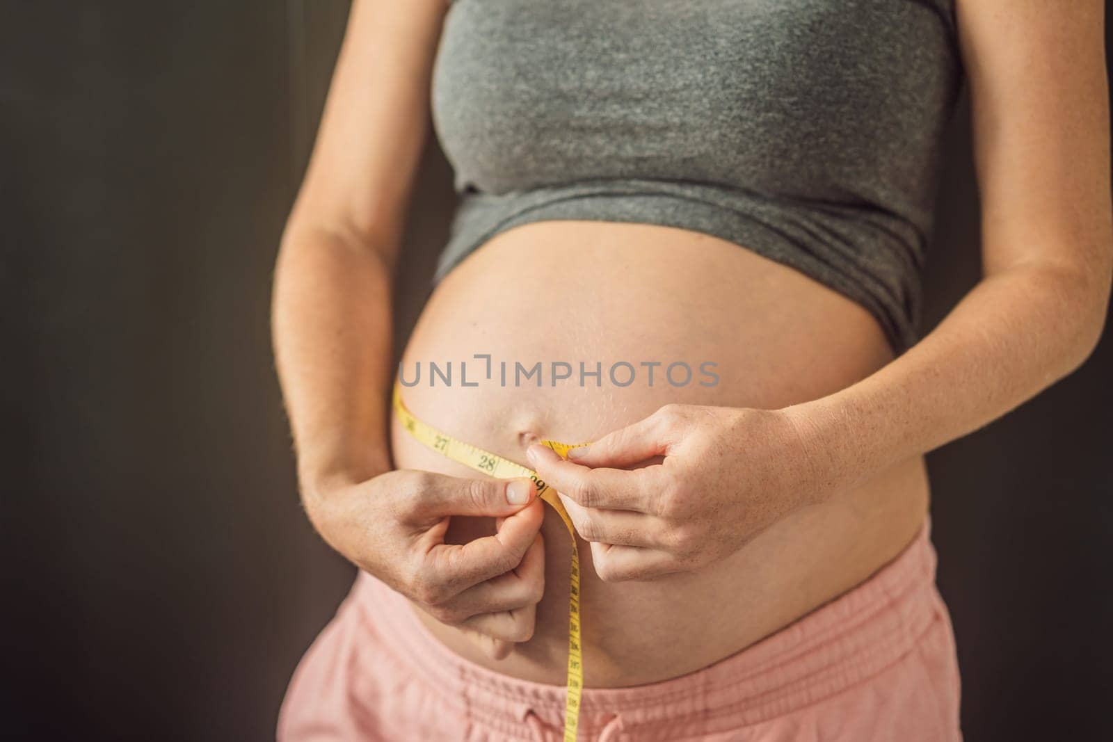 Young woman measuring her pregnant belly with inch tape. Inches, American standard. Preparation for childbirth, Girl big belly advanced healthy pregnancy.