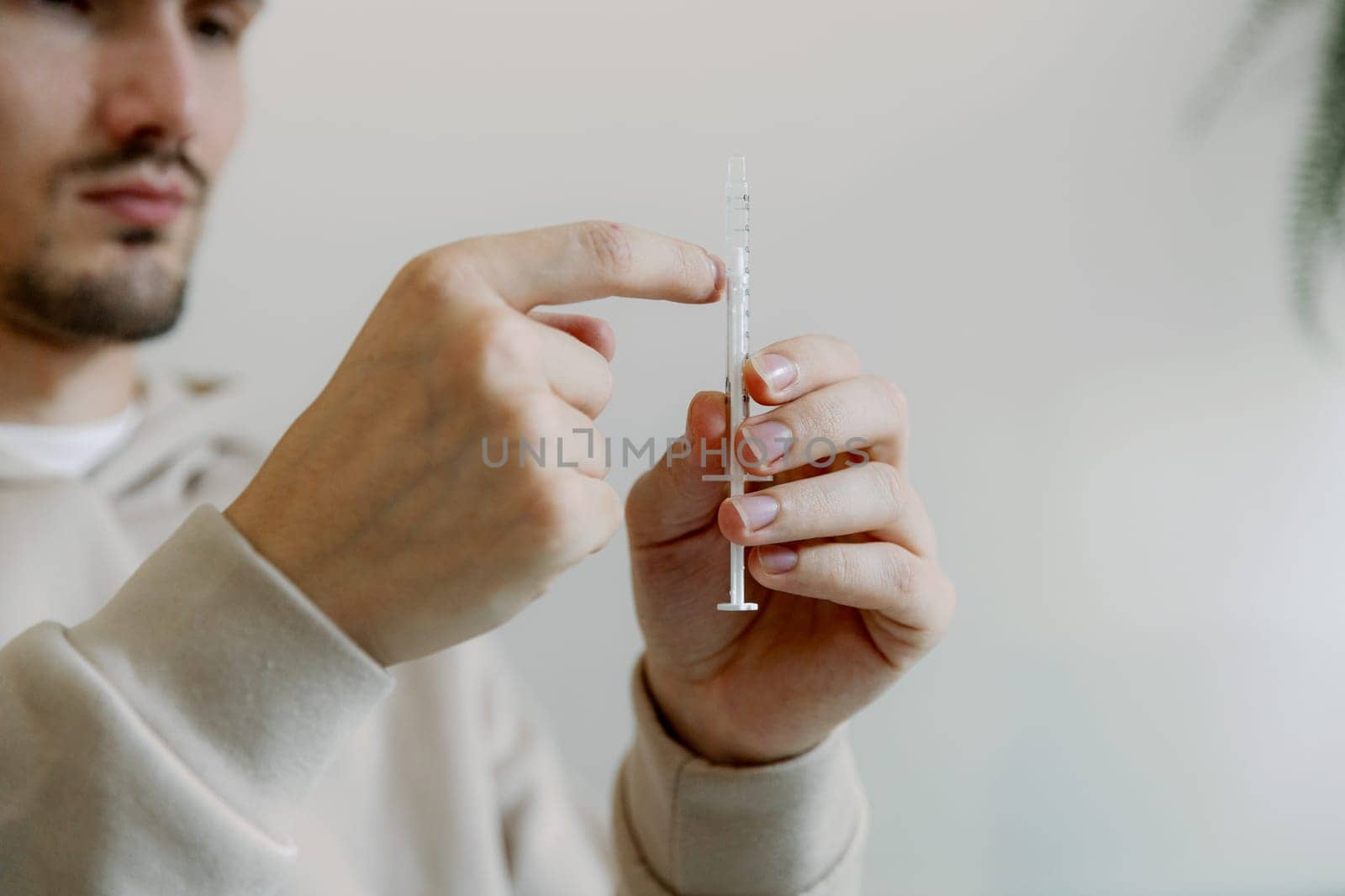 One young Caucasian handsome brunette man shakes a syringe with medicine with his fingers to get rid of air bubbles to treat his cat at home, close-up side view.