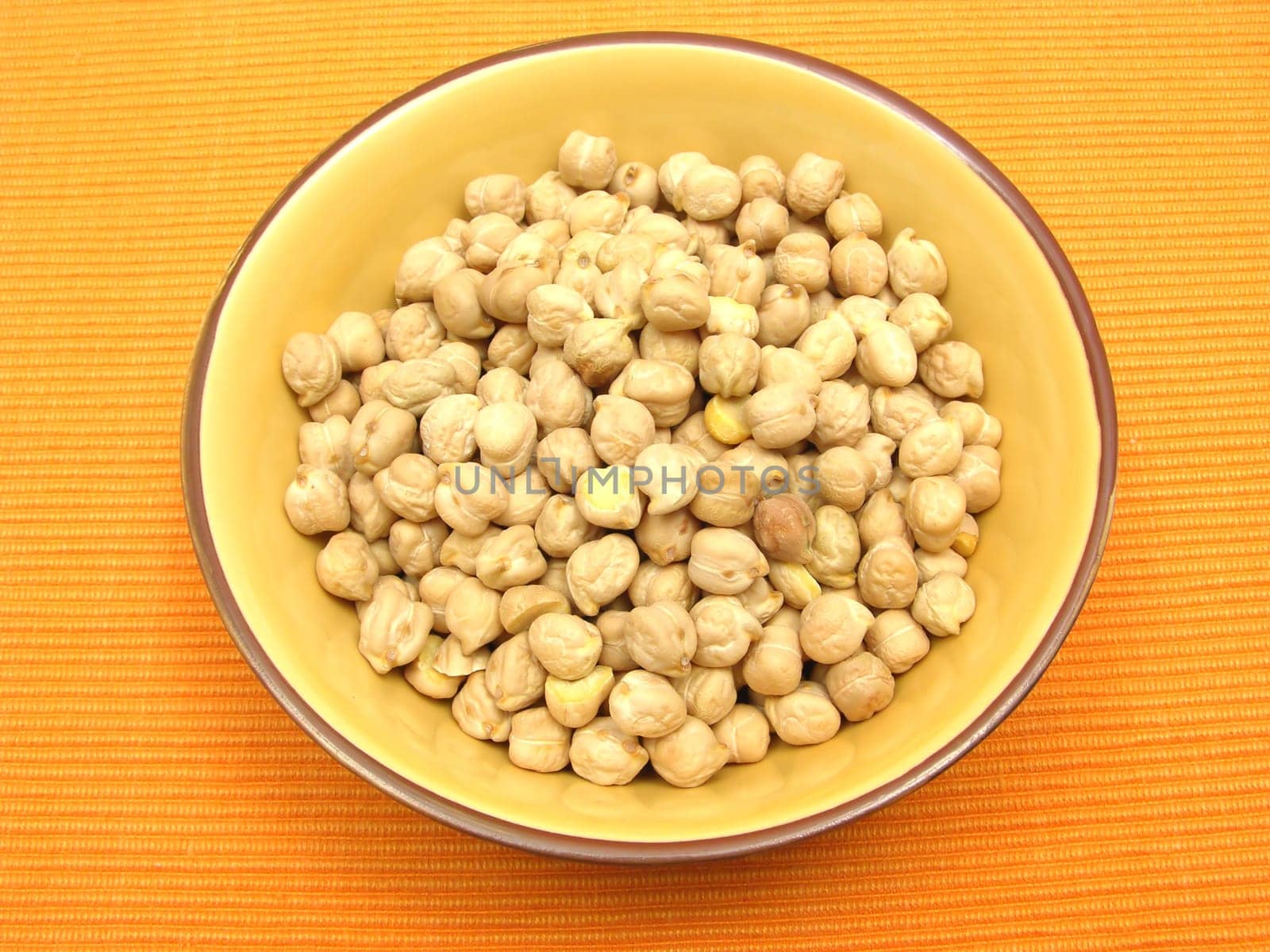 A ceramic bowl with chickpeas on an orange background