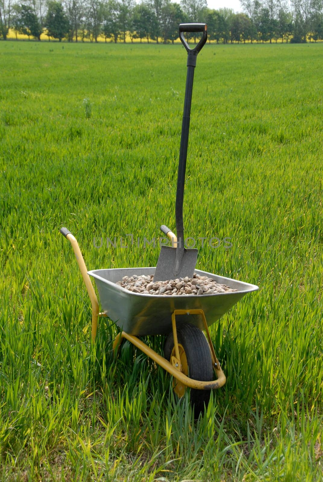 Wheelbarrow with gravel and spade on field