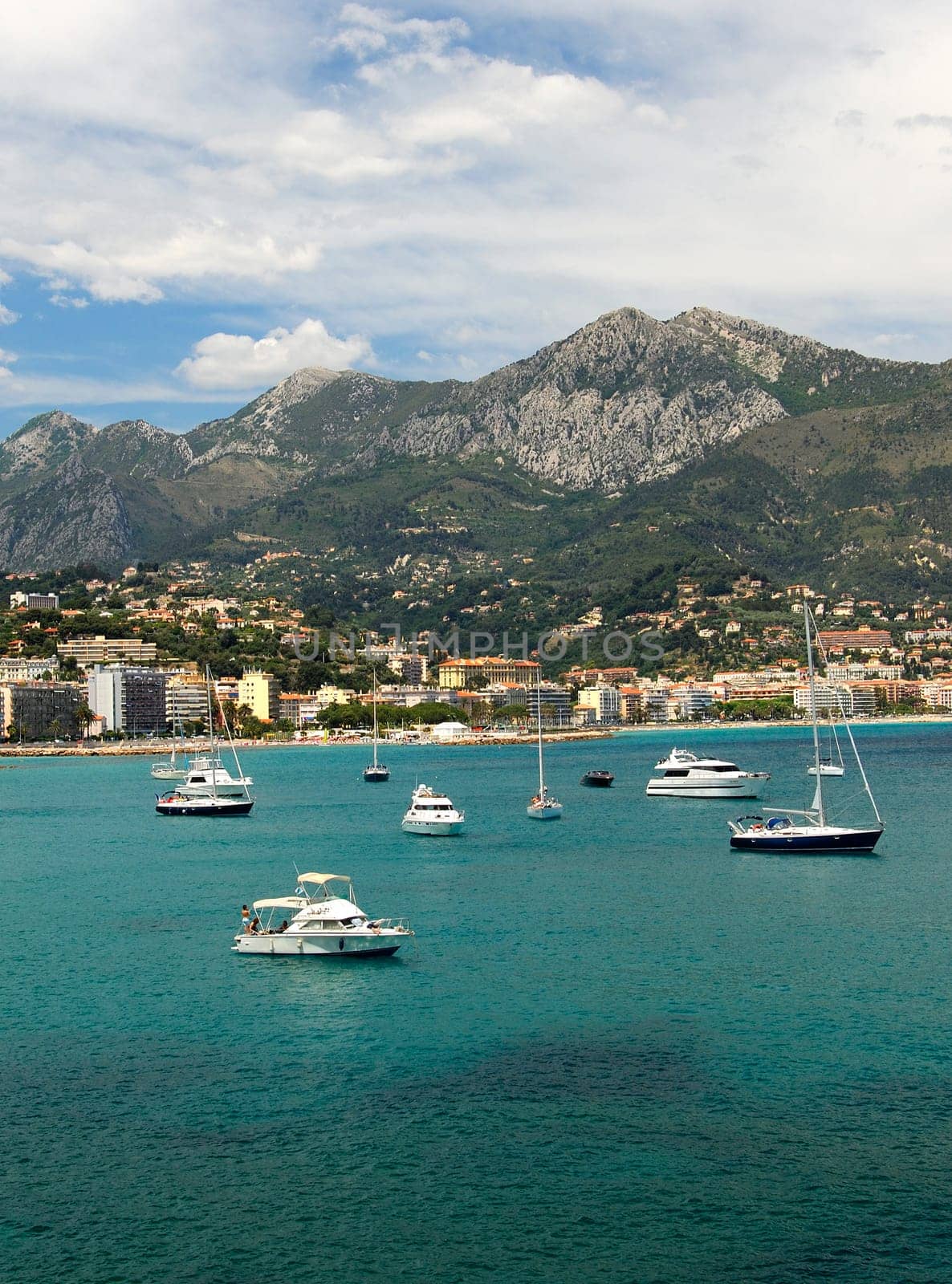 Sailing yachts and motorboats in the bay of Menton in front of the French mountain ranges