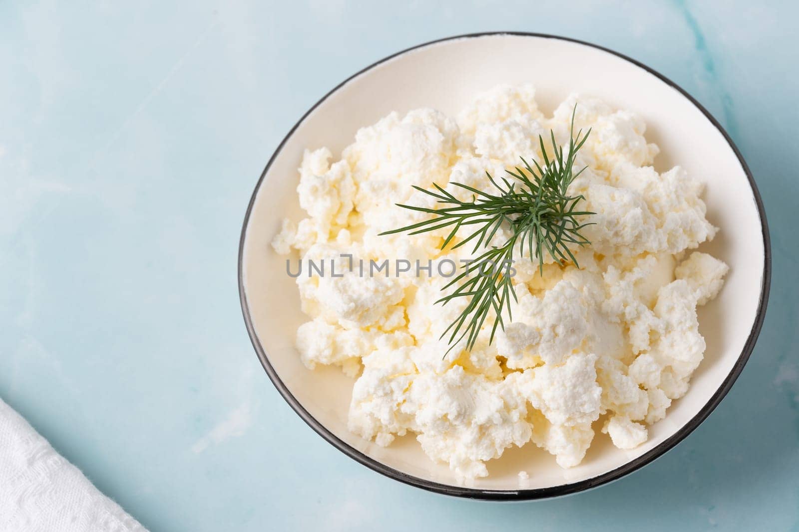 Fresh cottage cheese served in a bowl garnished with herbs on a clean kitchen surface.