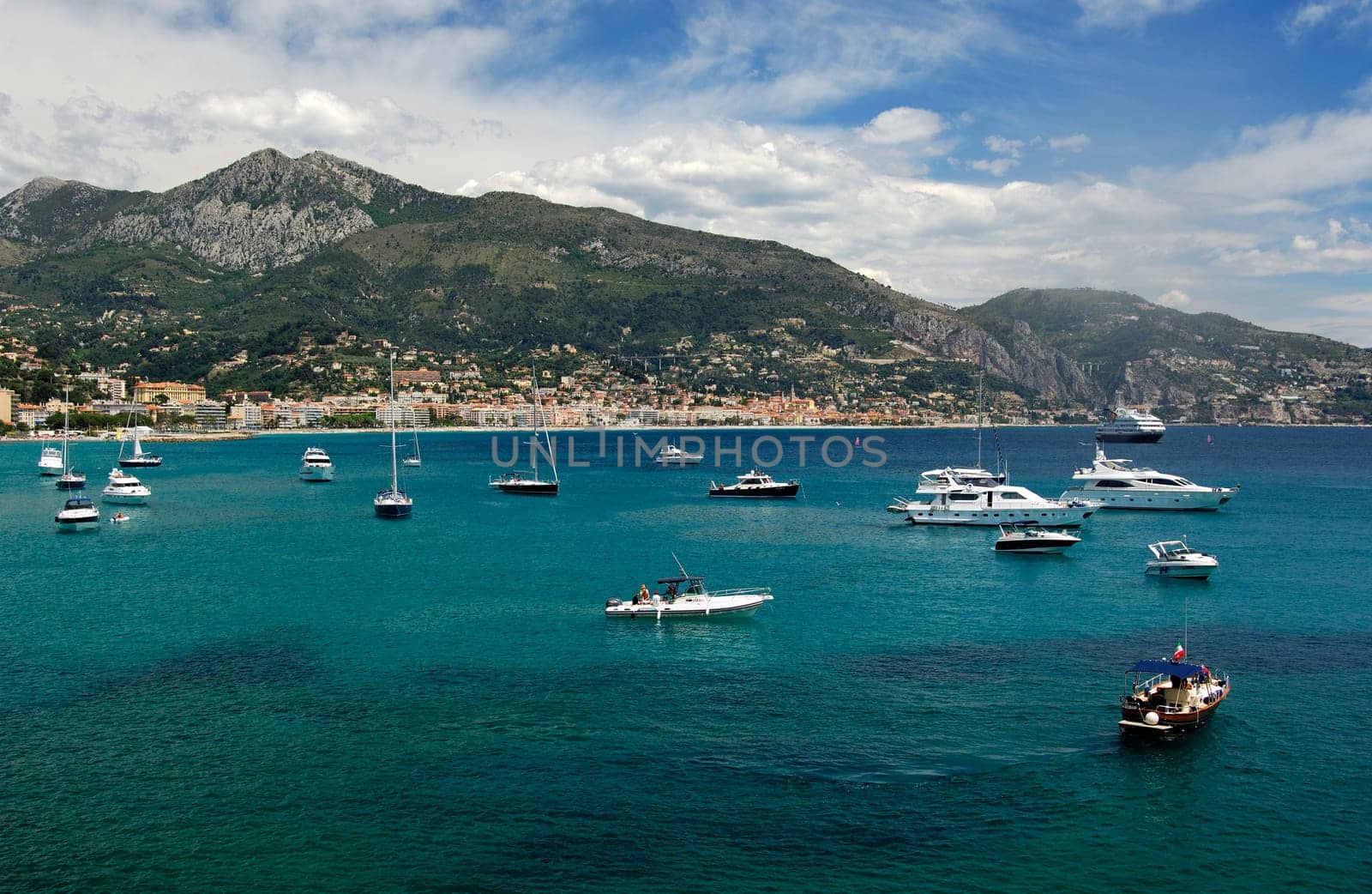 Sailing yachts and motorboats in the bay of Menton in front of the French mountain ranges