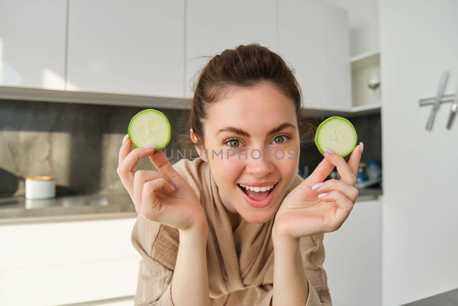 Food and lifestyle concept. Beautiful woman cooking in the kitchen, holding raw zucchini and smiling, preparing healthy vegetarian meal, making salad, looking happy.