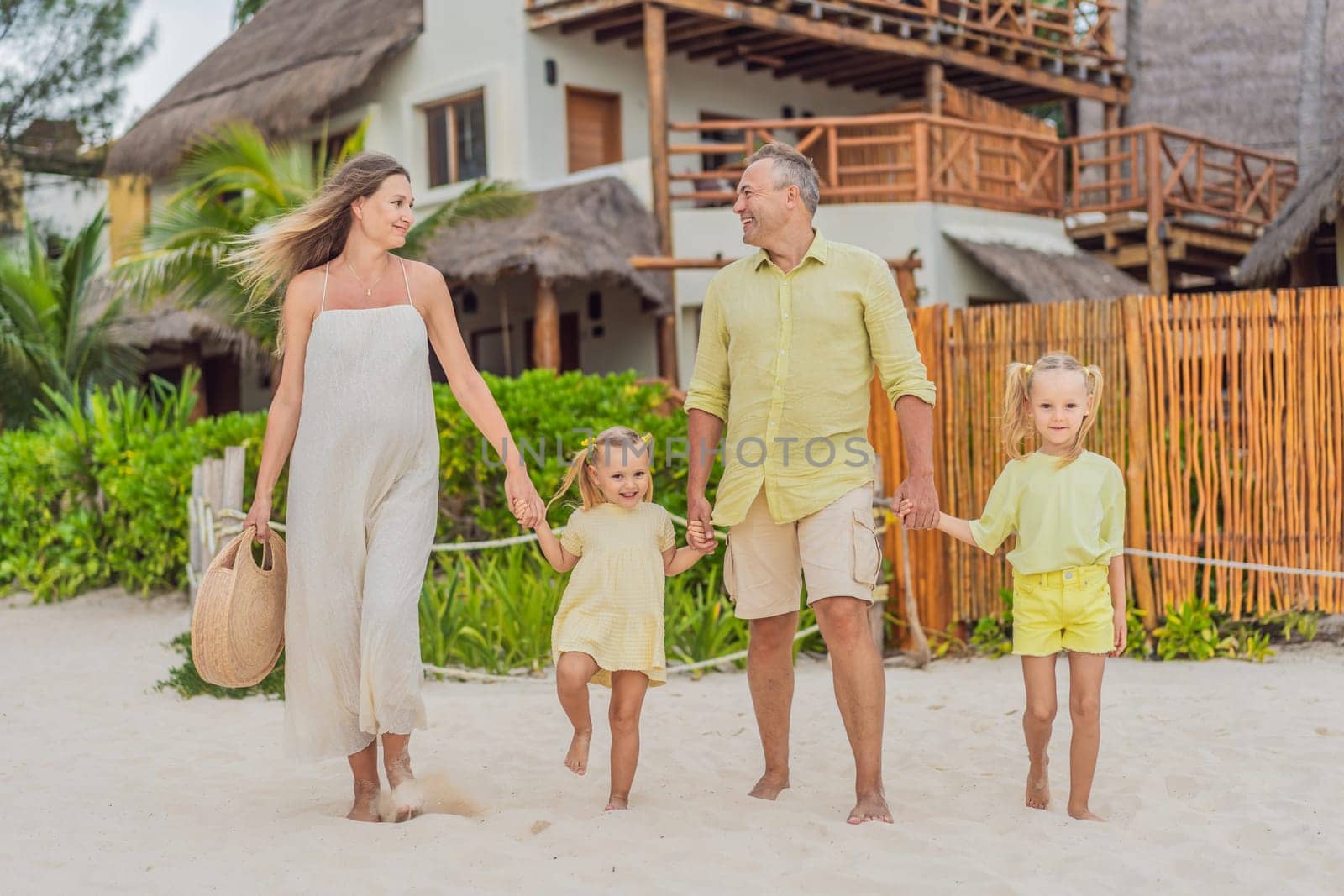 A joyful family, two girls, dad, and a pregnant mom, bask in tropical beach bliss, celebrating a radiant pregnancy amidst paradise.