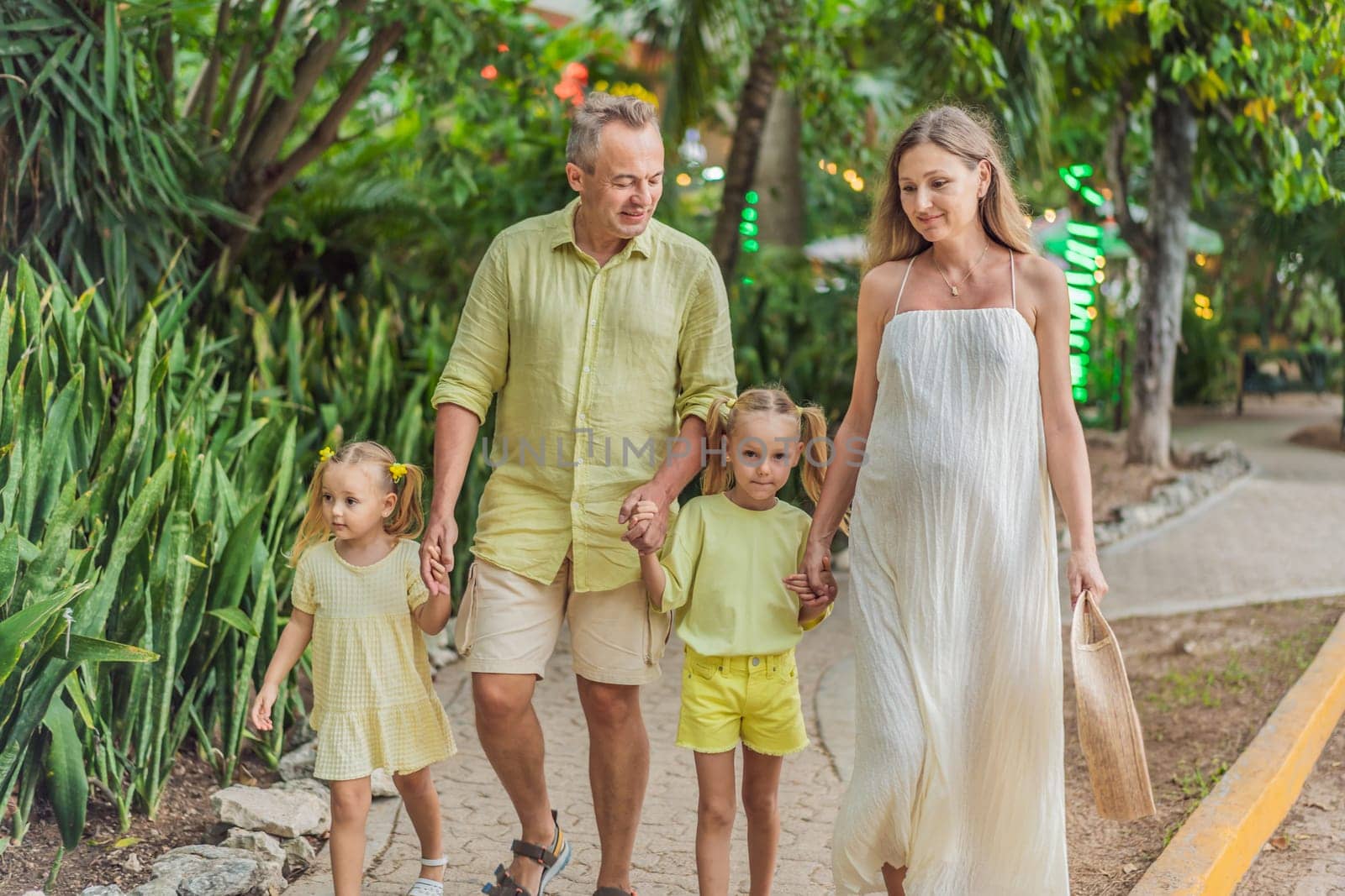 A joyful family, two girls, dad, and a pregnant mom, bask in tropical resort, celebrating a radiant pregnancy amidst paradise.