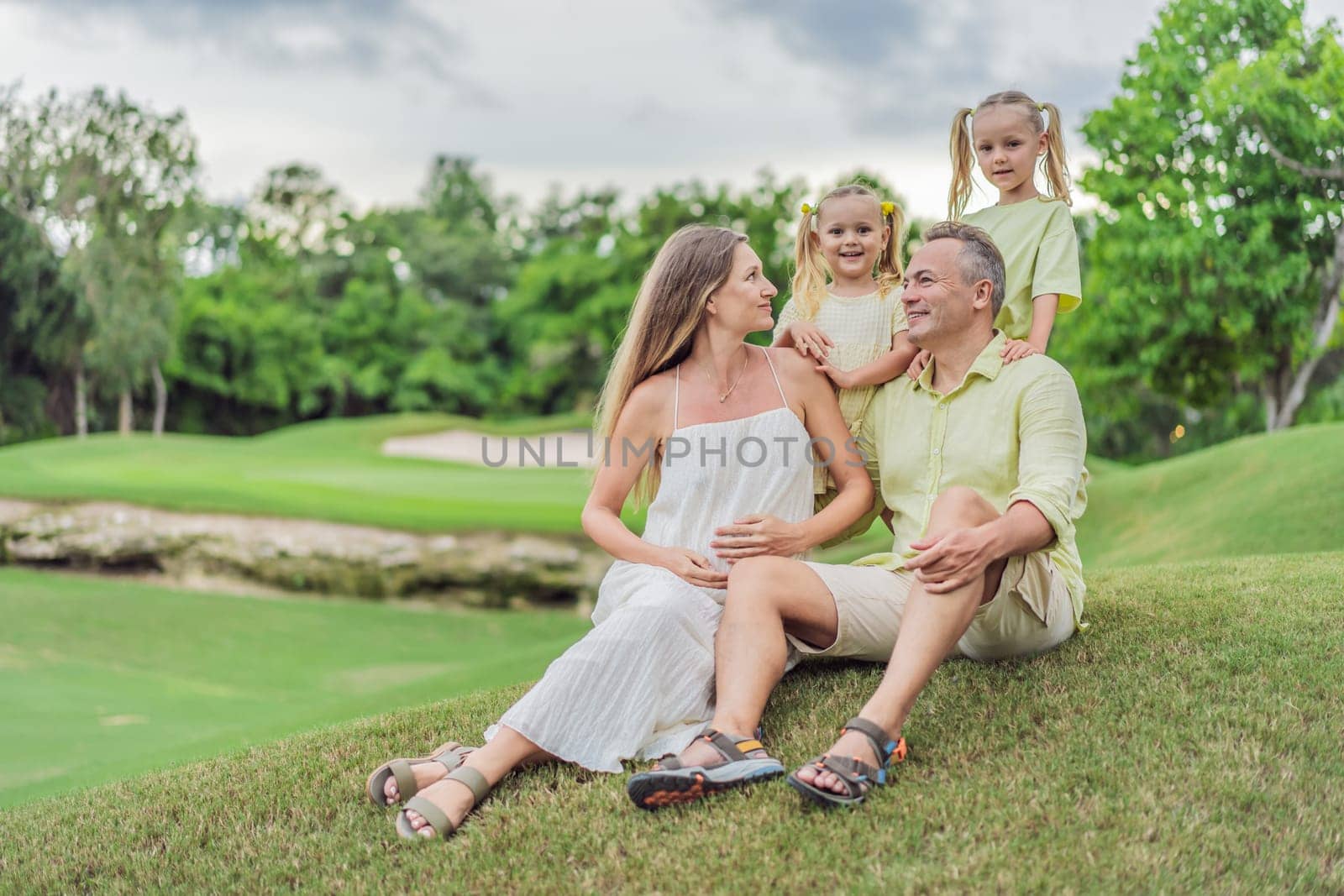 A happy family, two girls, dad, and a pregnant mom, enjoys quality time together on a lush green lawn, creating cherished memories of togetherness by galitskaya
