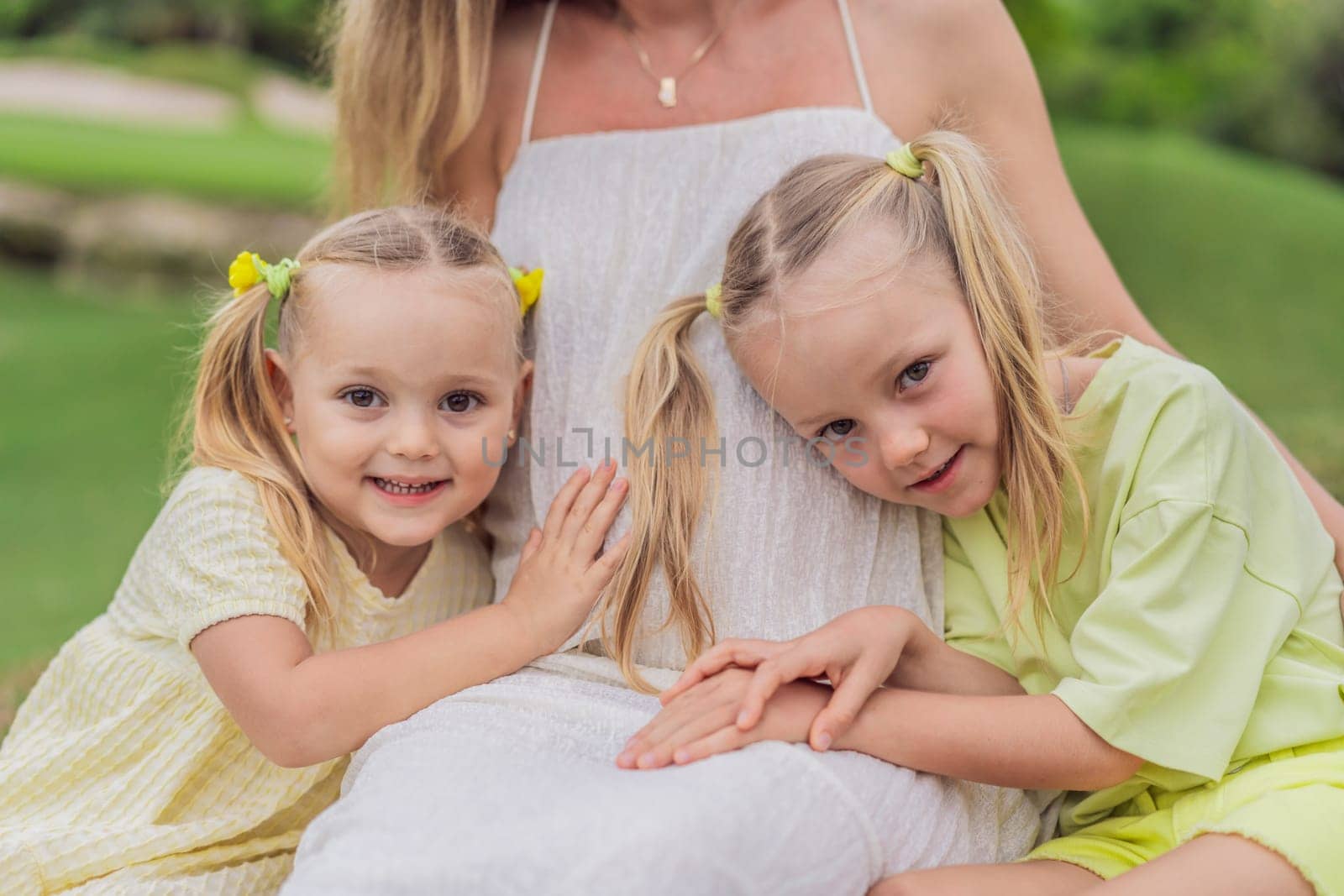 Sisters' love blooms as they tenderly embrace their mother's pregnant belly, sharing anticipation and affection for their soon-to-arrive sibling.