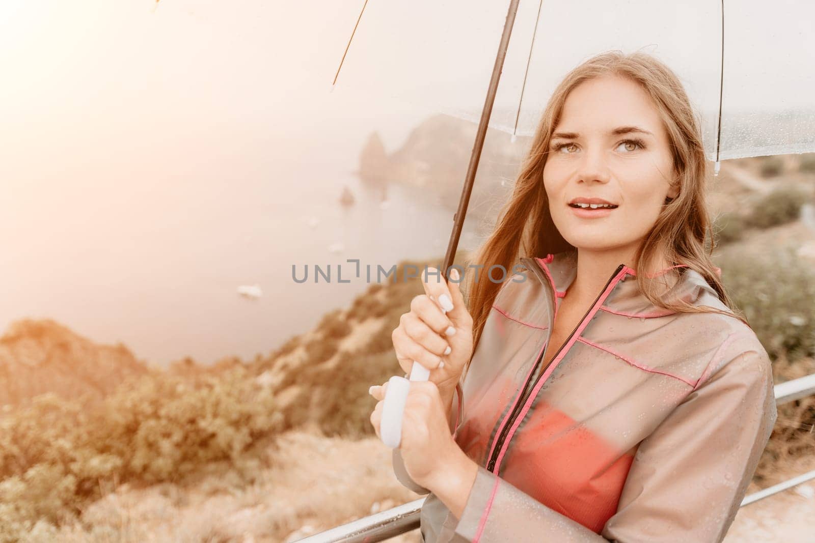 Woman rain park. Happy woman portrait wearing a raincoat with transparent umbrella outdoors on rainy day in park near sea. Girl on the nature on rainy overcast day