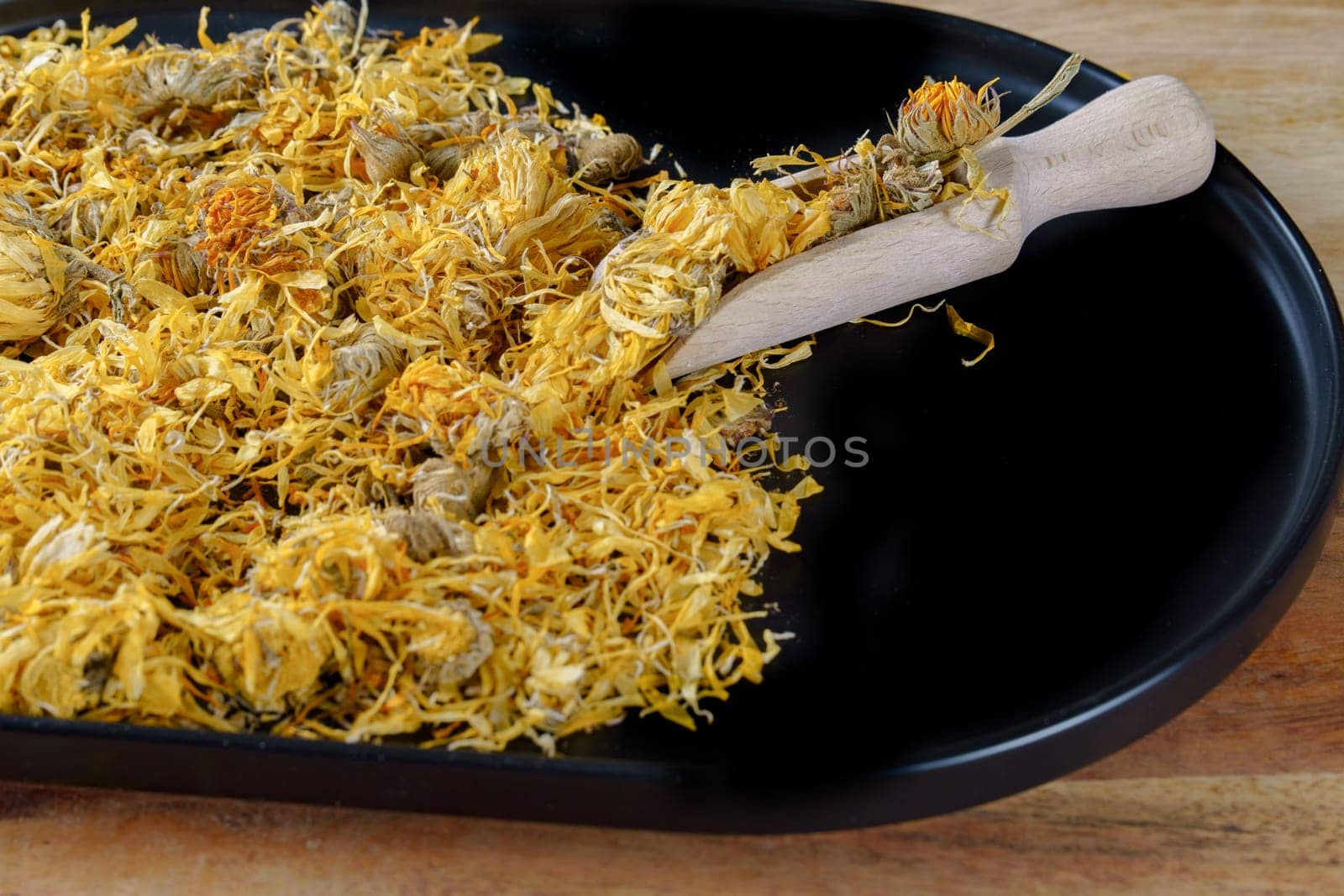 dried flowers of calendula, Calendula officinalis, in a wooden spoon on a black tray. Medicinal plant for therapeutic use,