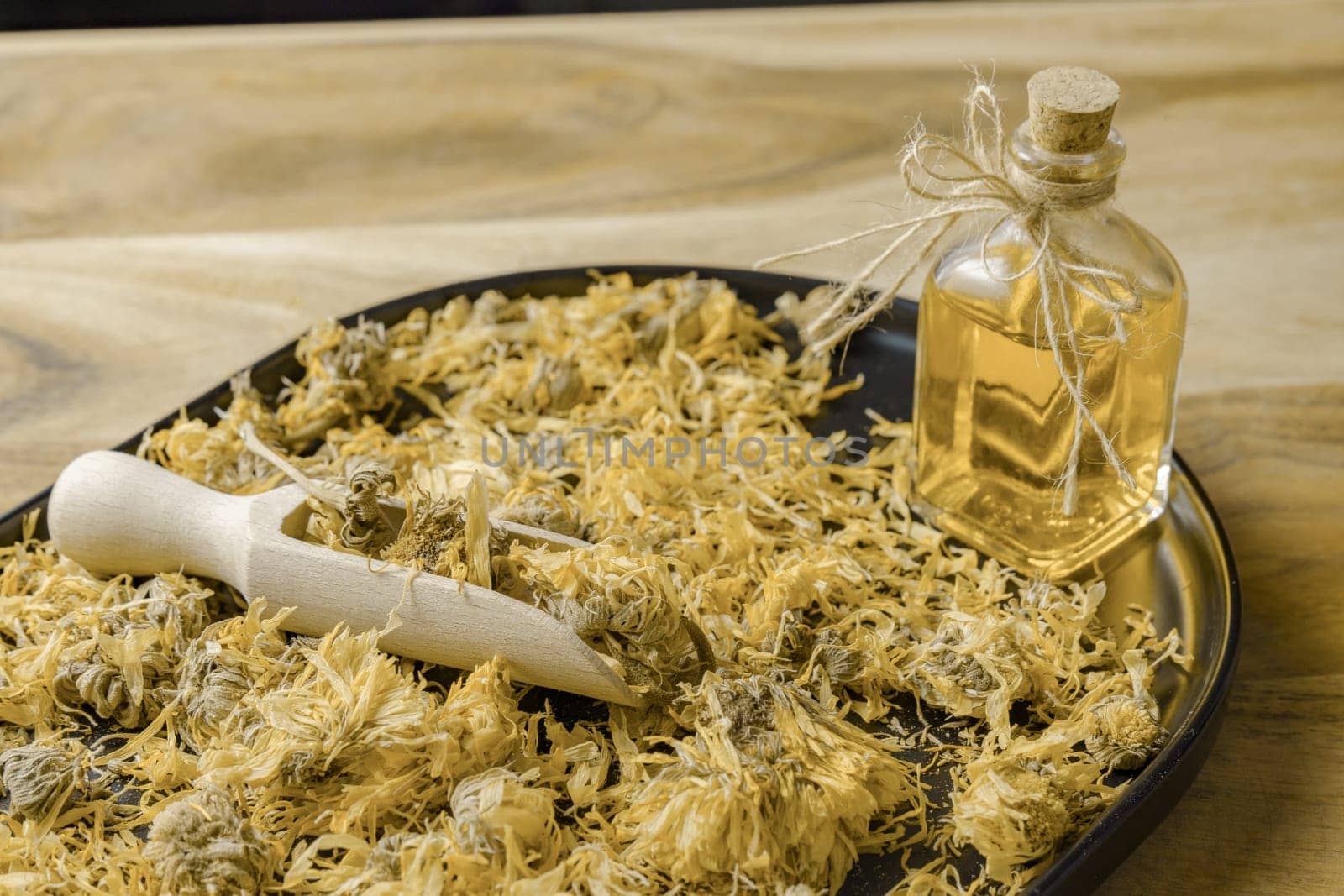 dried calendula flowers, Calendula officinalis, medicinal plant for therapeutic use, in a black tray with a bottle of calendula essential oil.