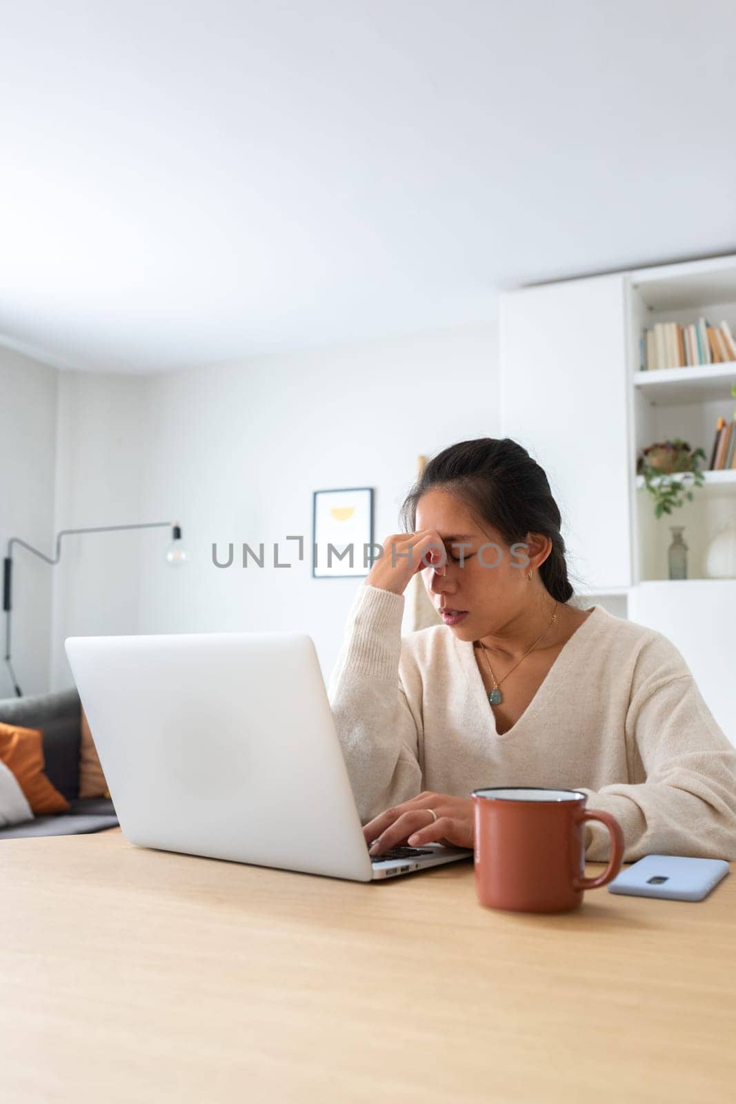 Vertical portrait of young Asian woman feeling tired and having headache after working long hours at home office. by Hoverstock