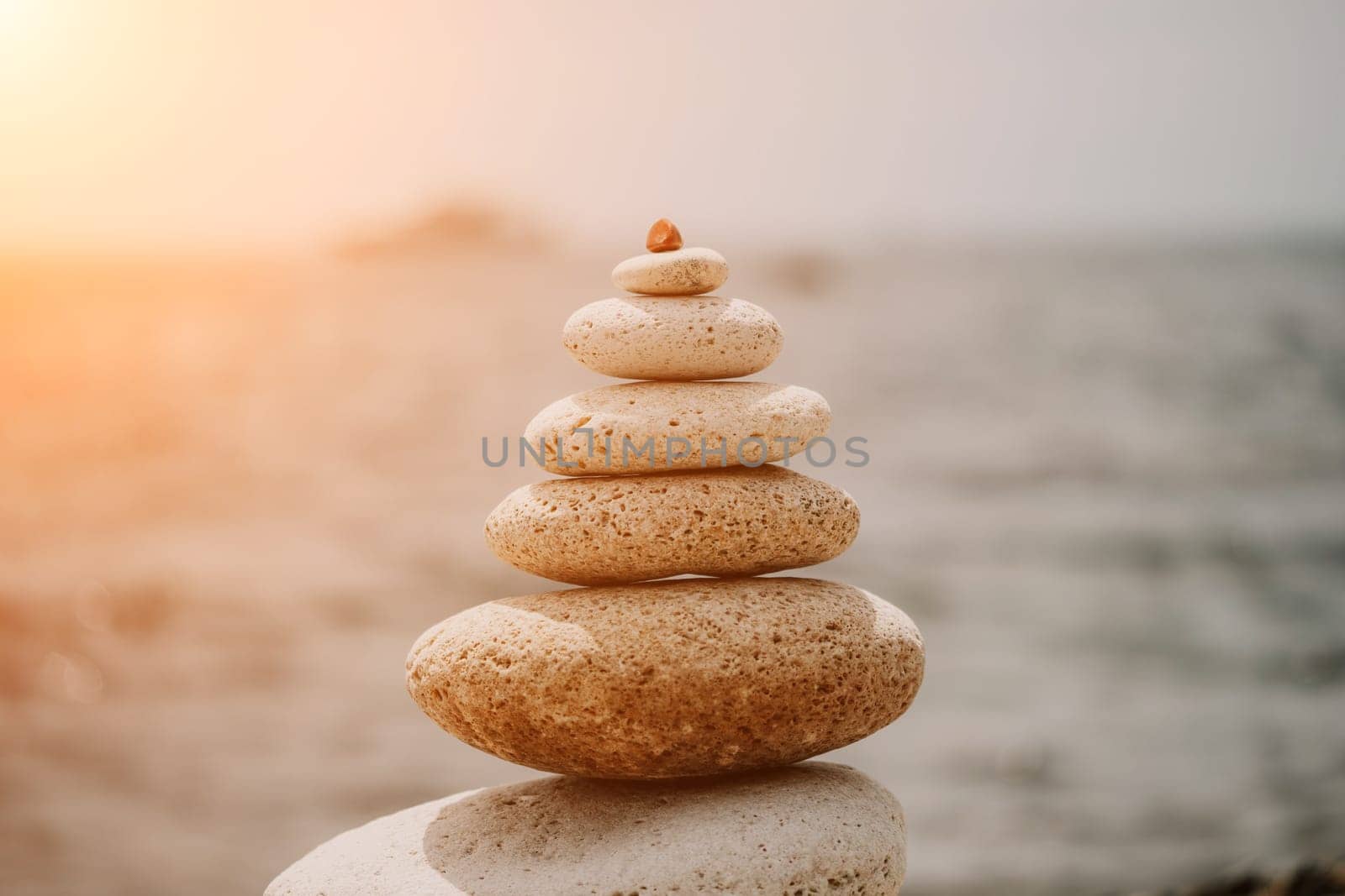 Zen stones and balanced rock pyramid on pebble beach at sunset. Golden sea bokeh on background. Concept of harmony, meditation, spa, calmness, balance. by panophotograph