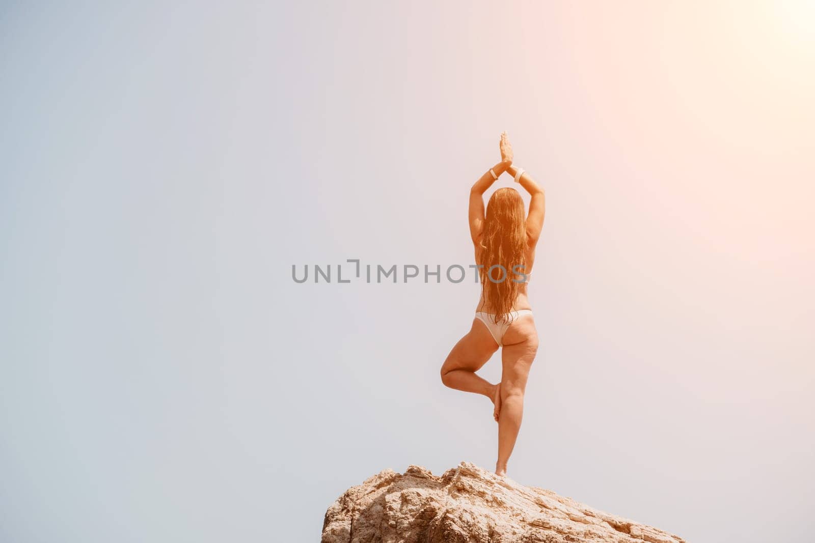 Woman sea yoga. Back view of free calm bliss satisfied woman with long hair standing on top rock with yoga position against of sky by the sea. Healthy lifestyle outdoors in nature, fitness concept. by panophotograph