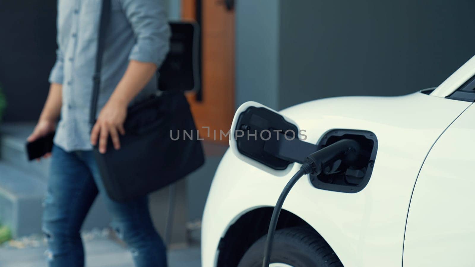 A man unplugs the electric vehicle's charger at his residence. Concept of the use of electric vehicles in a progressive lifestyle contributes to a clean and healthy environment.