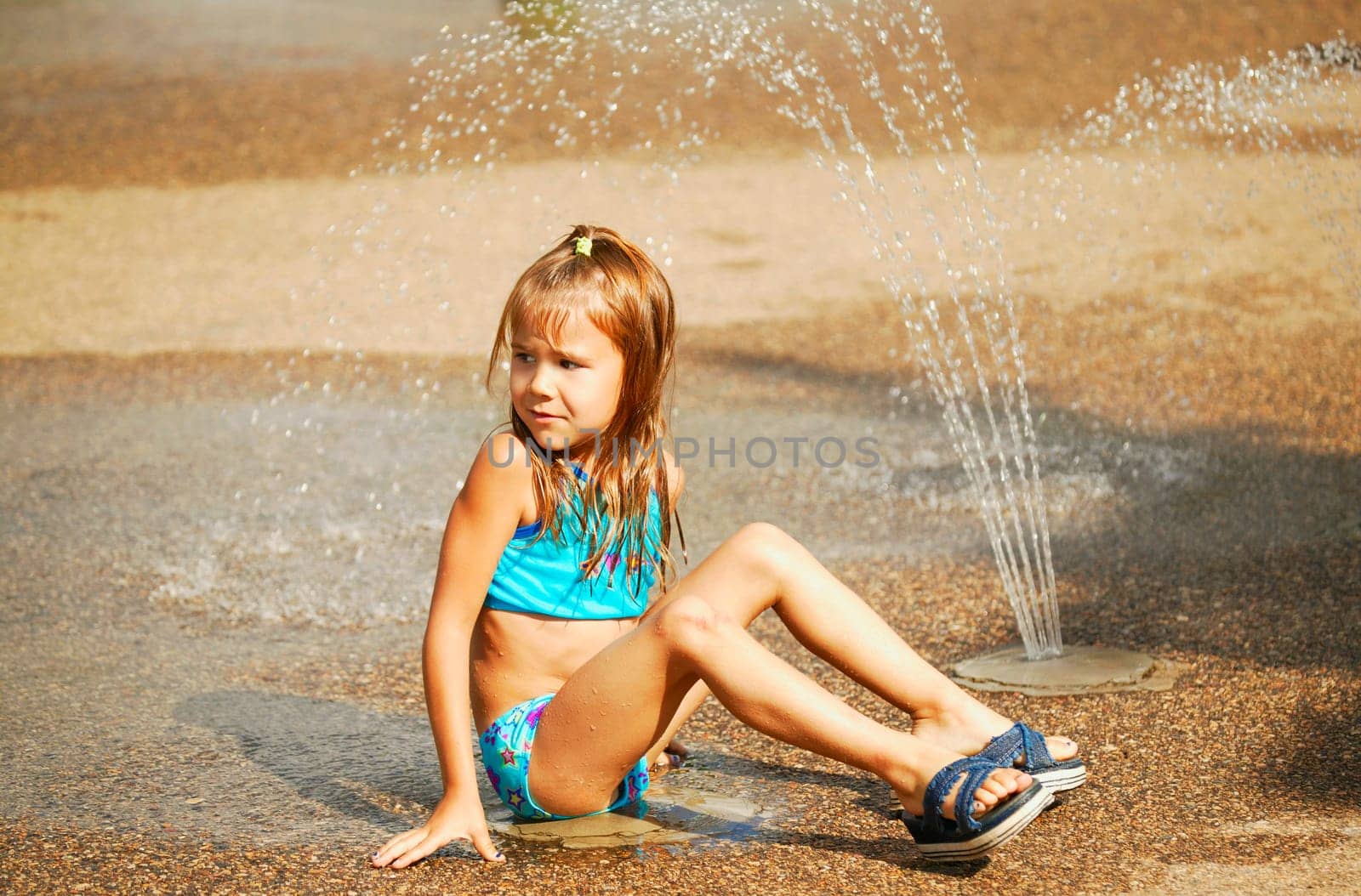Child sits beside sprinkler